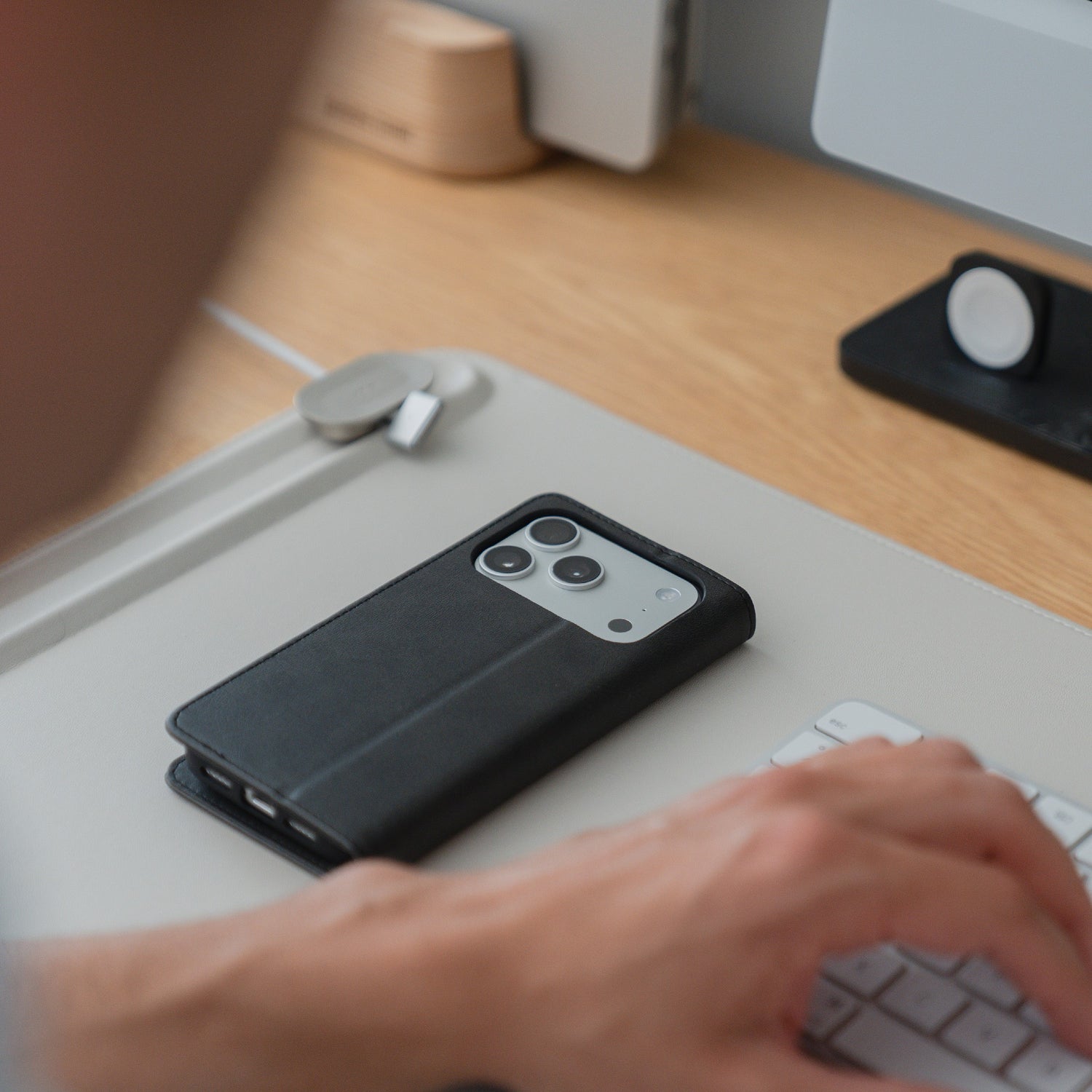 Person tippt auf einer Tastatur, daneben ein Smartphone in der eleganten arktis iPhone 17 Pro Book Case Kunstlederhülle auf dem Schreibtisch - die perfekte Hülle von arktis für das iPhone 17 Pro.