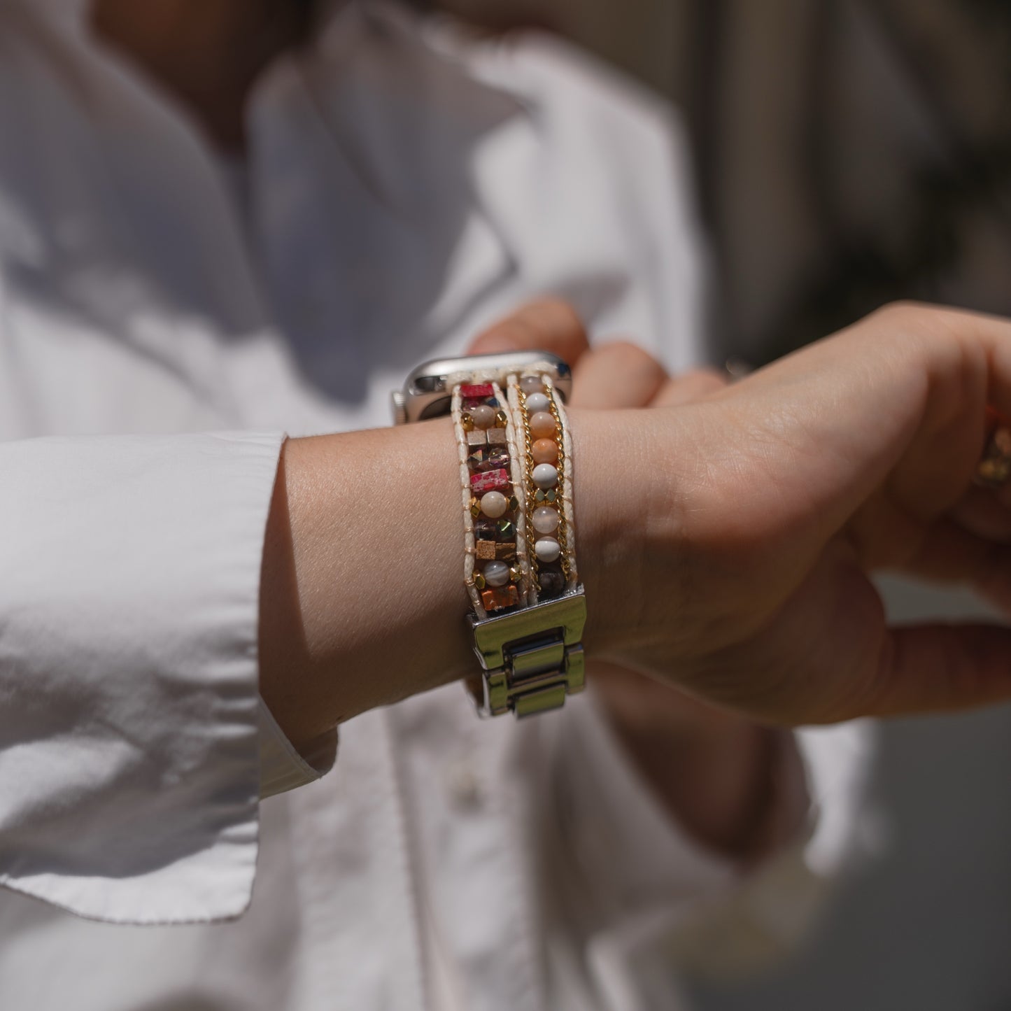 Eine Person in einem weißen Hemd richtet ihr Arktisband Apple Watch-Armband „Sunset Spirit“ von Arktisband zurecht und präsentiert dessen stilvolles Perlen-Design, das mit der Apple Watch kompatibel ist.