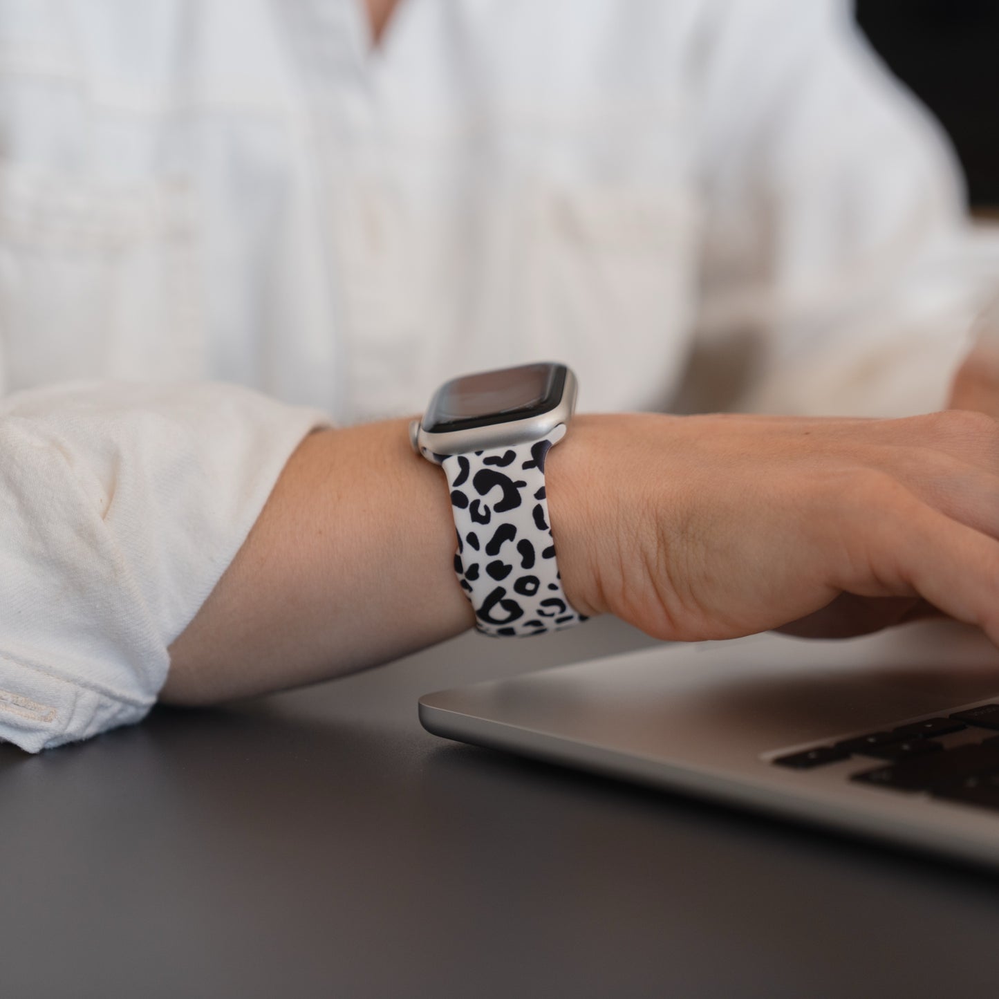 Eine Person, die ein arktisband Snow Leopard Apple Watch Armband von arktisband mit schwarzem und weißem Leopardenmuster trägt, tippt auf einem Laptop.