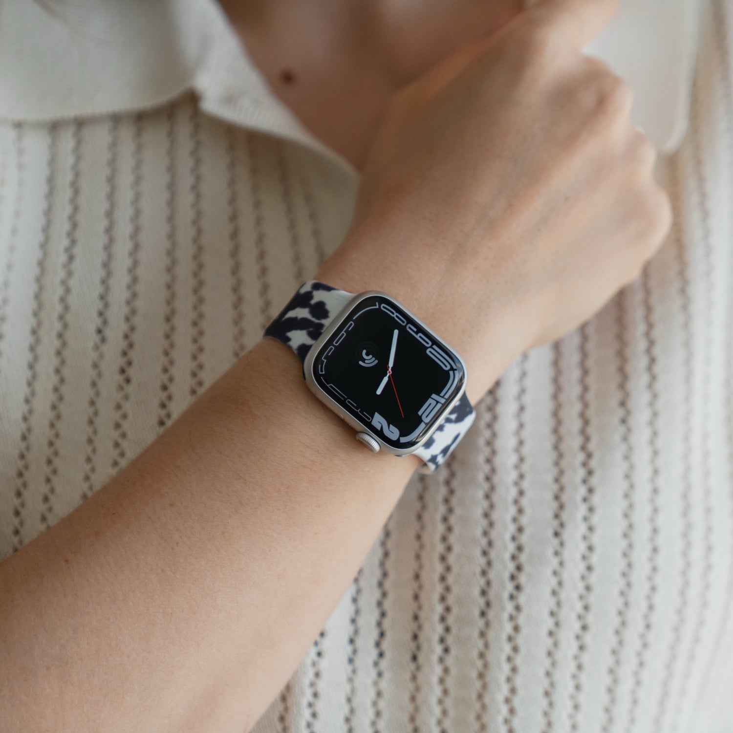 Jemand, der ein „Kuhfell“-Apple-Watch-Armband von arktisband an seiner Apple Watch trägt, dazu ein cremefarbenes Strickhemd.