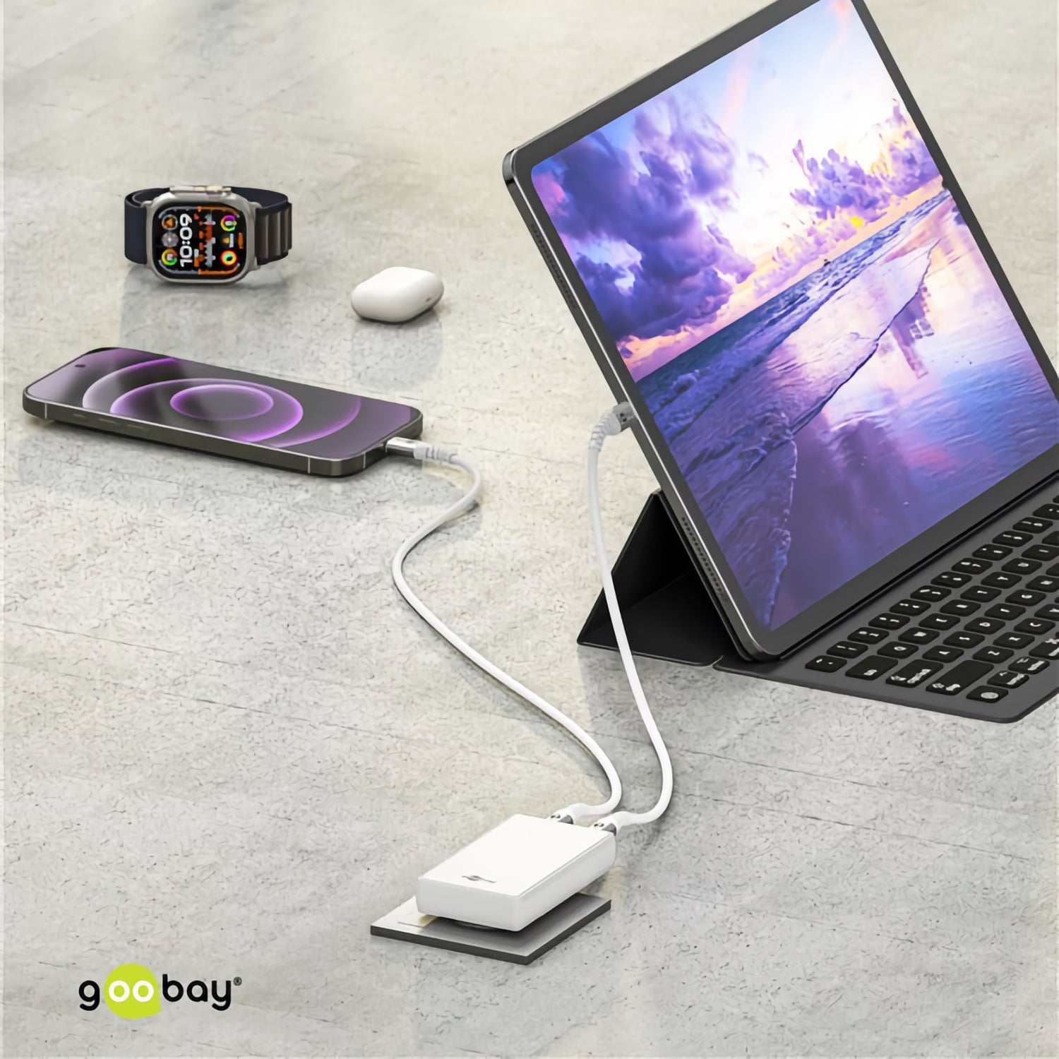 Tablet, Smartphone, Smartwatch und Earbuds werden mit dem Goobay USB-C Dual-Schnellladegerät 90° Flat 65 W und einer portablen Powerbank auf eine graue Oberfläche geladen.