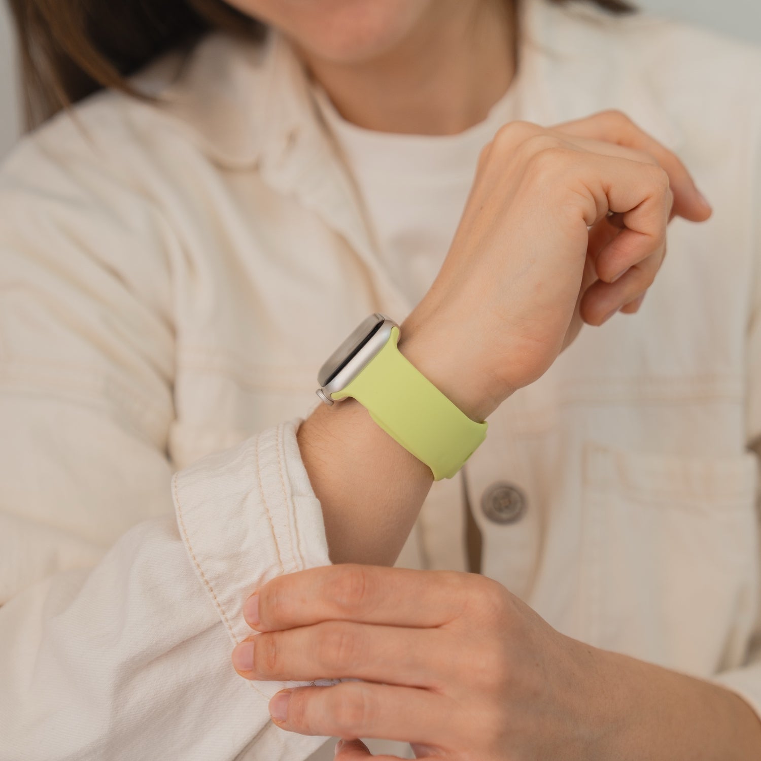 Eine Person, die ein Arktisband Apple Watch Silikonarmband "Sport" in Hellgrün trägt, verstellt den Ärmel ihres cremefarbenen Hemdes.