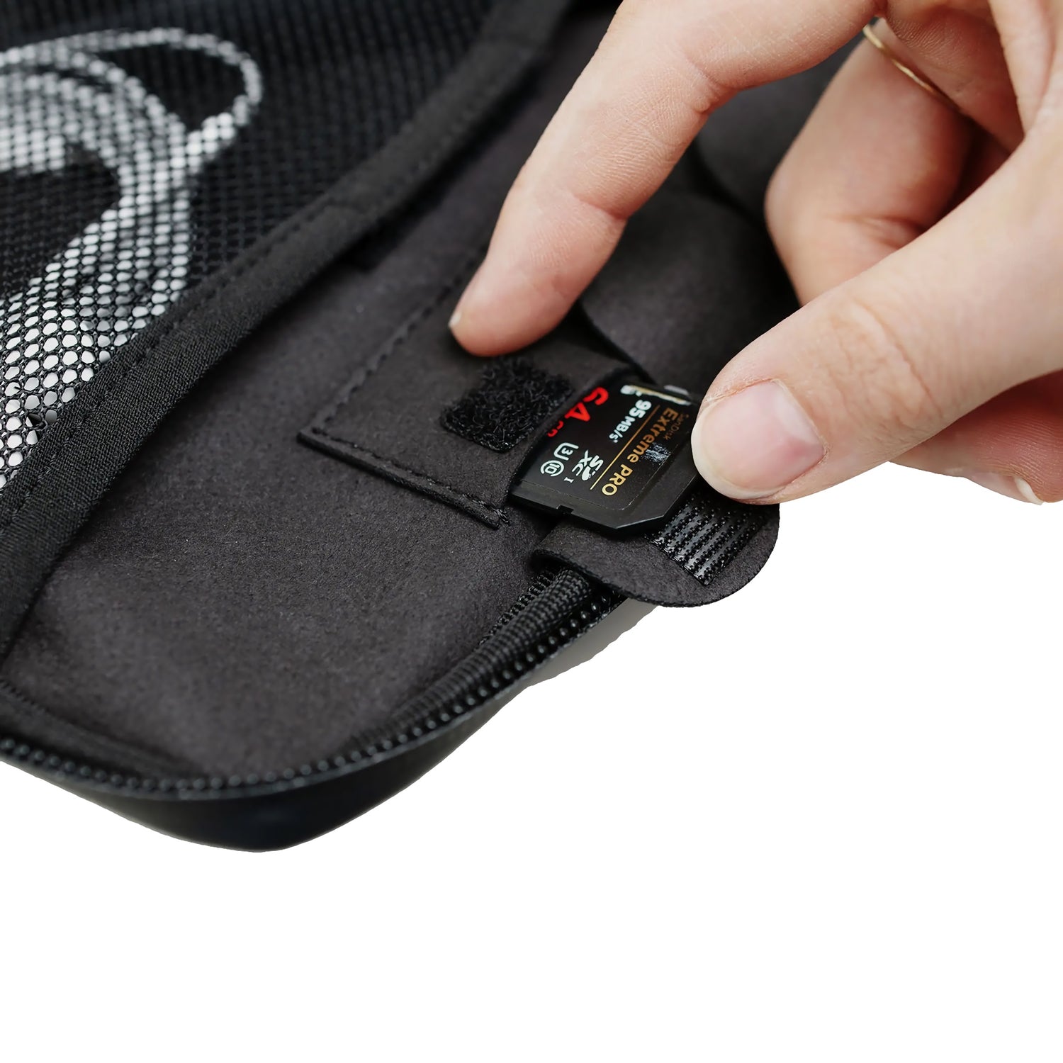 Eine Hand steckt eine SD-Karte in die Netztasche einer schwarzen MOMENT Wetterfestes Mobile Lens Carrying Case für 4 Linsen, konzipiert für praktische Organisation und als wetterfeste Kameraausrüstung.