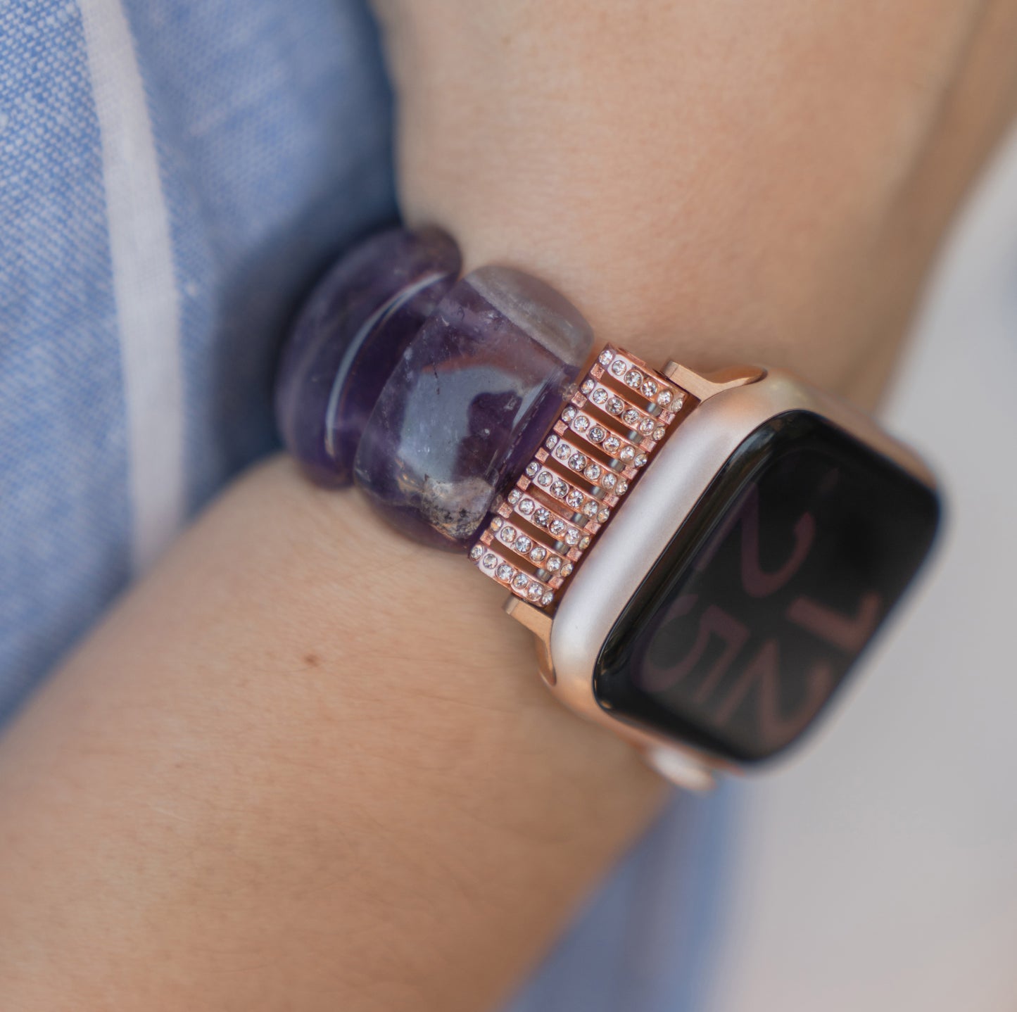Am Handgelenk einer Person schmückt eine Apple Watch „Stone Pearl“ von arktisband mit einem mit Edelsteinen besetzten Armband und einem klobigen violetten Stein-Armband.