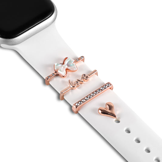 Ein weißes Arktisband-Smartwatch-Armband ist mit vier roségoldenen Arktisband-Apple-Watch-Charms „Love Bow“ versehen: einem Schmetterling, einem „Love“-Anhänger, einem Kristallstab und einem Herz. Der Rand des exklusiven Accessoires ist oben links teilweise sichtbar.