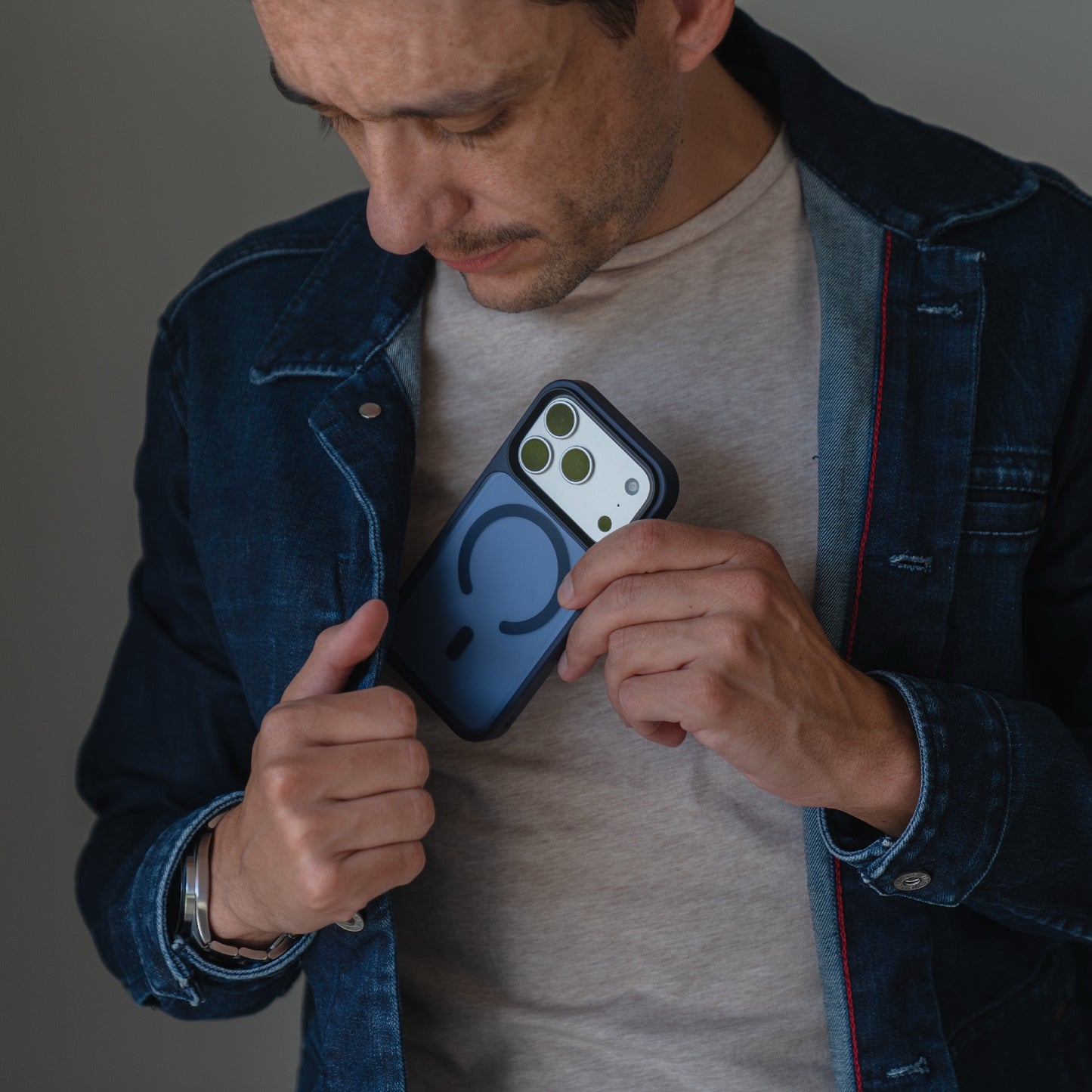 Ein Mann steckt sein iPhone 17 Pro in einem Arktis Solid Case mit MagSafe (blau-matt) in die Innentasche seiner Jeansjacke.