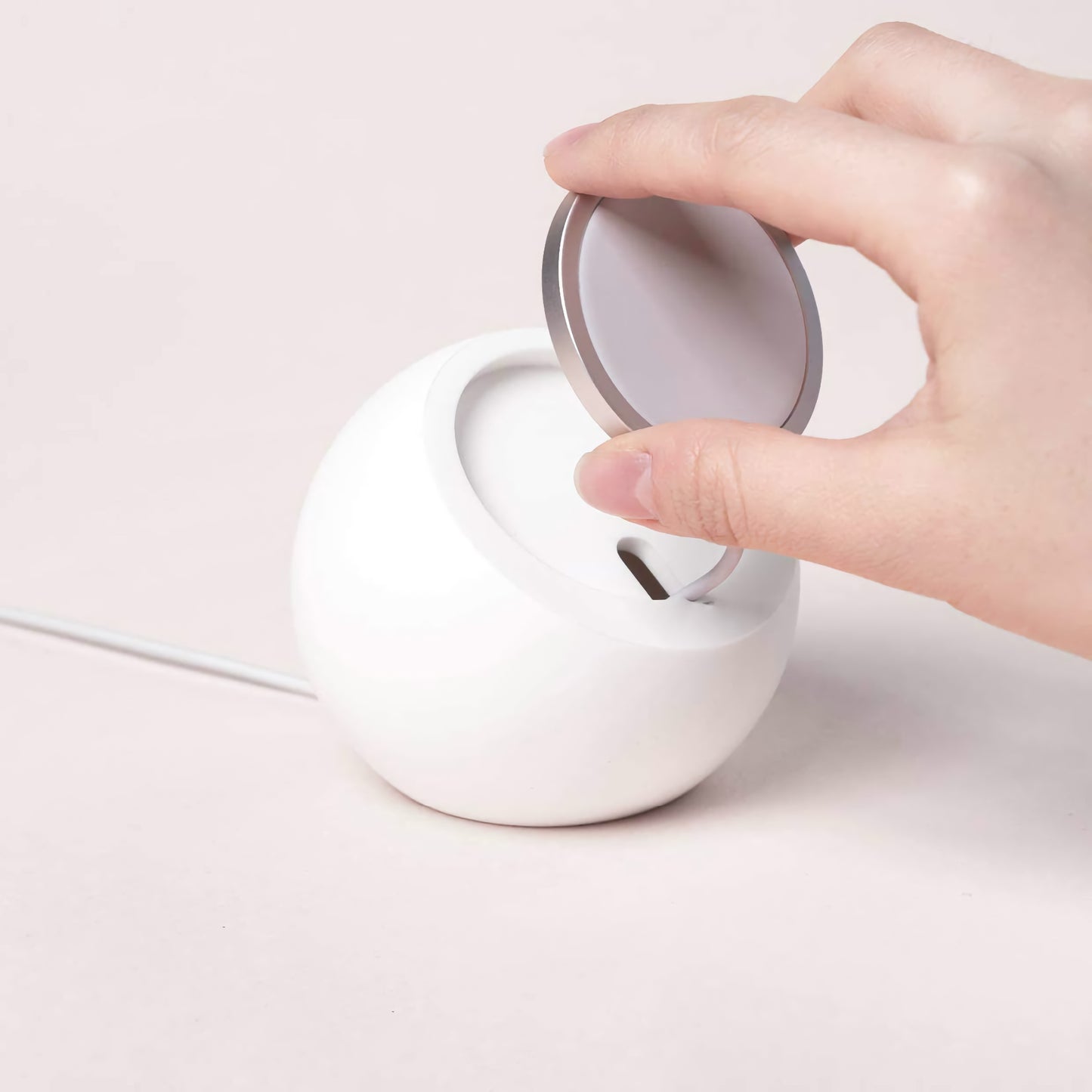 Eine Hand stellt den arktis MagSafe Orbit Stand von arktis auf eine weiße, runde Ladestation auf einer hellen Fläche für kabelloses Laden.