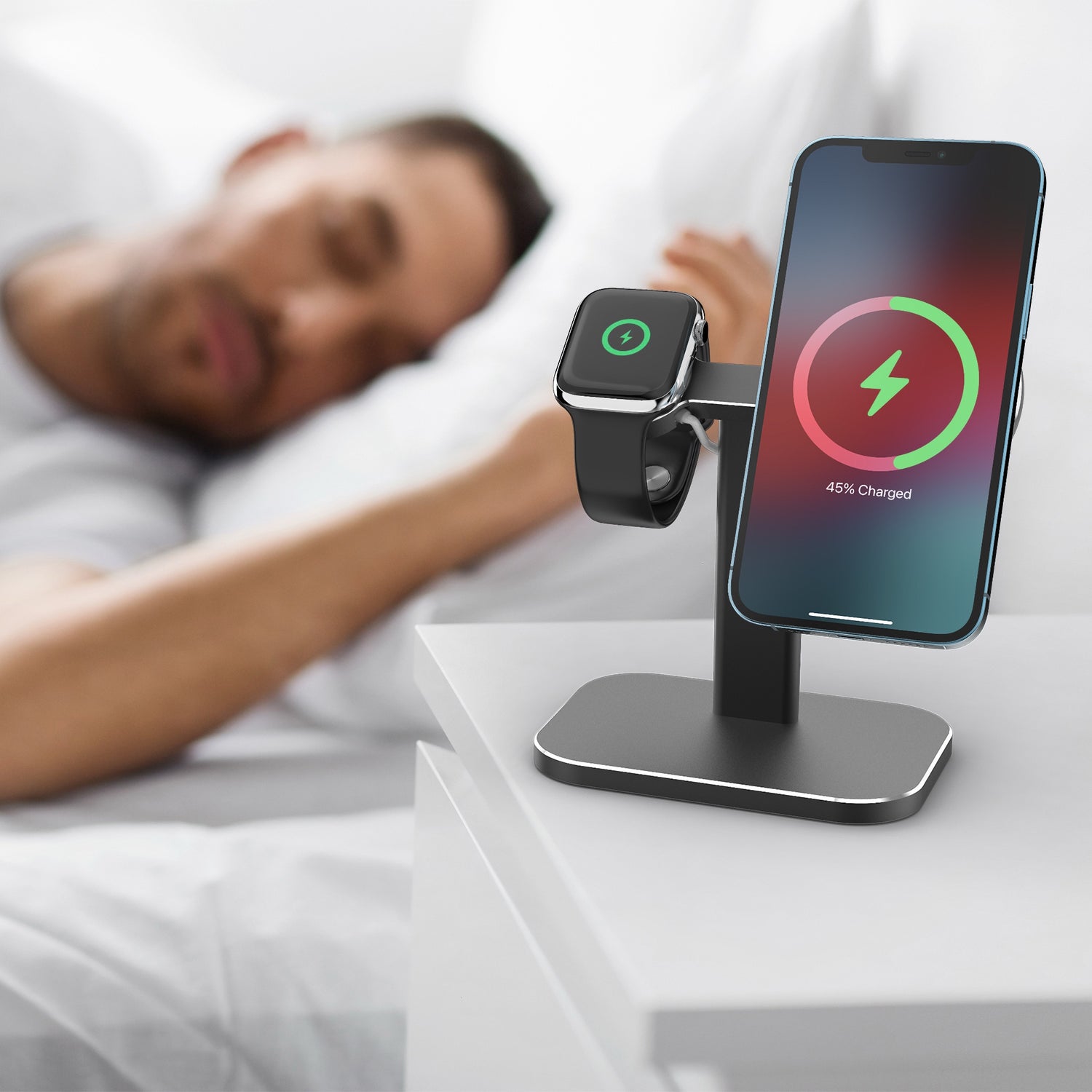 Ein iPhone und eine Apple Watch werden auf dem arktis MagSafe AluStand von arktis aufgeladen, der neben einem Mann im Bett liegt.