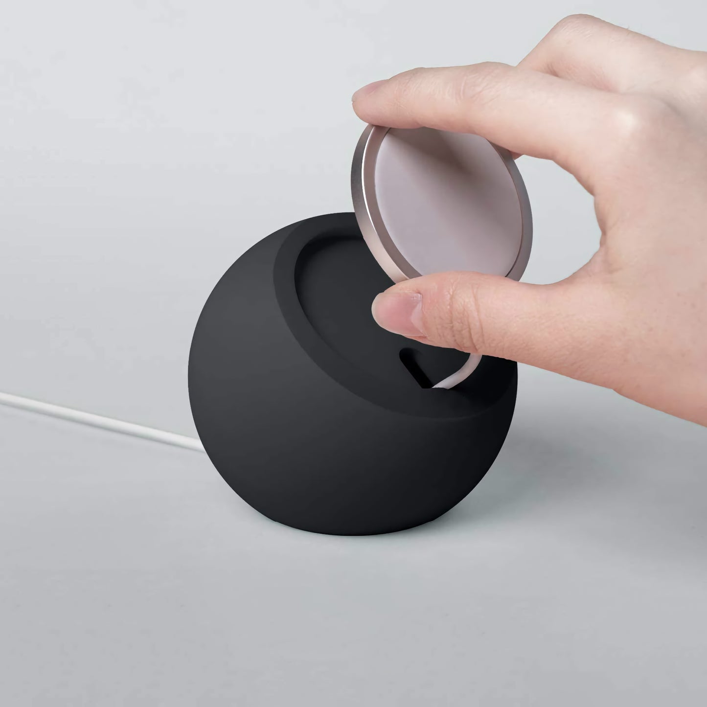 Eine Hand setzt ein rundes Gerät auf die schwarze arktis MagSafe Orbit Stand Ladestation mit angeschlossenem Kabel und demonstriert damit das kabellose Laden.