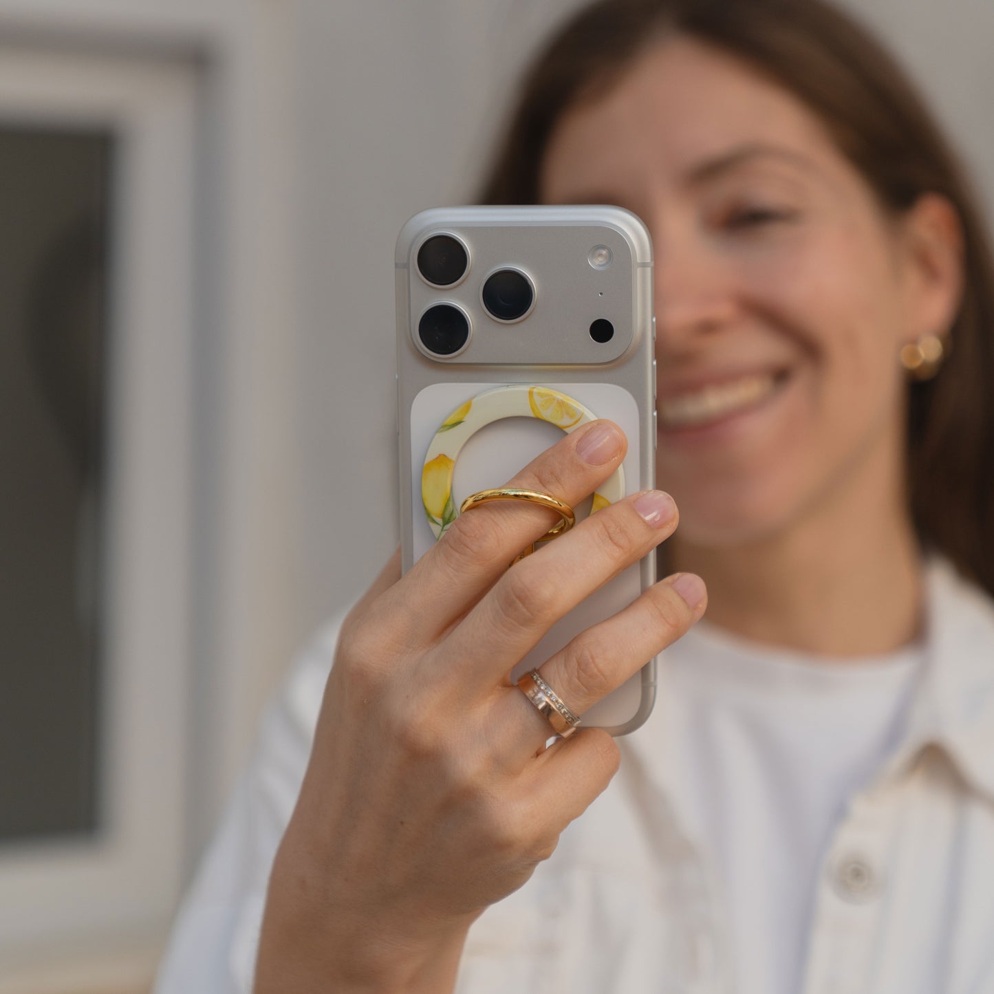 Eine Frau lächelt, während sie ihr Telefon mit dem arktis Magnetischer Ringhalter für MagSafe - Sweet Leopard hält. Sie zeigt ihren Goldring und ihr Ehering-stylisches iPhone Zubehör mit starken N52 Magneten für einen sicheren Halt.