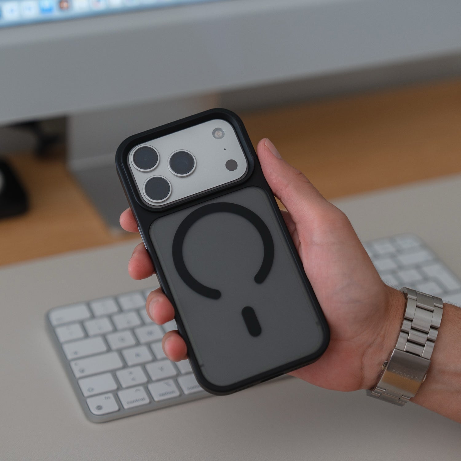 Eine Hand hält ein Arktis iPhone 17 Pro Solid Case mit MagSafe, ein mattes Gehäuse von Arktis, über einer weißen Tastatur und einem Schreibtisch.