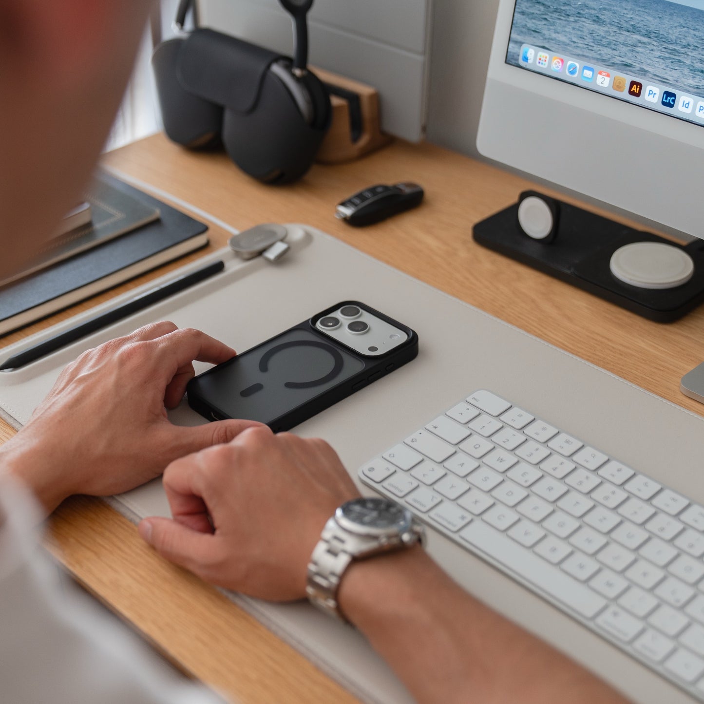 Eine Person sitzt an einem Schreibtisch mit einem Smartphone in einem Arktis iPhone 17 Pro Solid Case mit MagSafe, sowie einer Tastatur, einem Monitor und trägt eine silberne Armbanduhr.