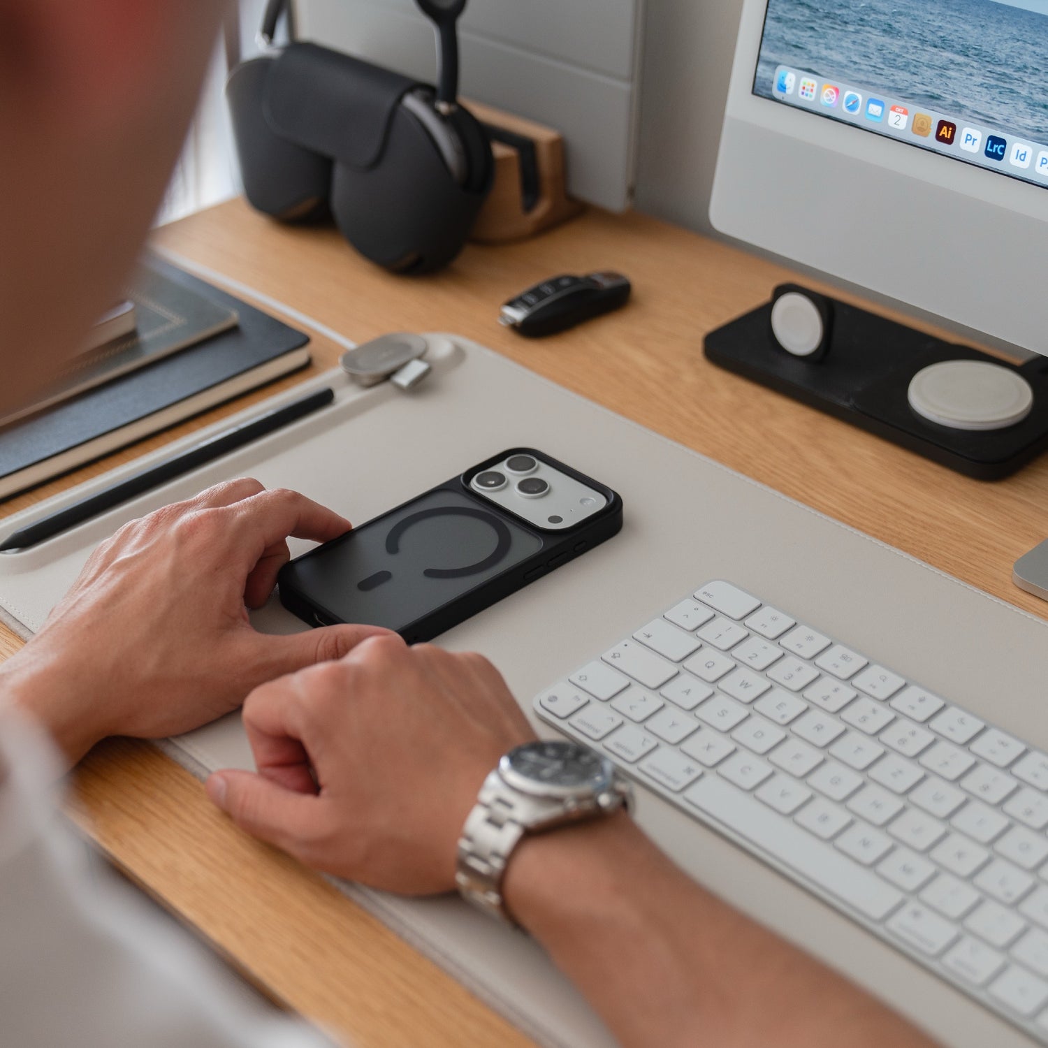 Eine Person sitzt an einem Schreibtisch mit einem Smartphone in einem Arktis iPhone 17 Pro Solid Case mit MagSafe, sowie einer Tastatur, einem Monitor und trägt eine silberne Armbanduhr.