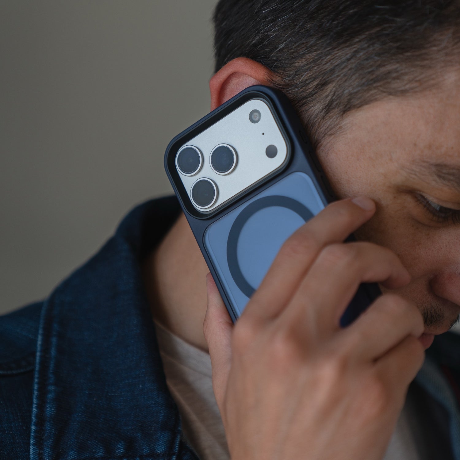 Eine Person in Jeansjacke hält sich ein iPhone 17 Pro mit dem Arktis iPhone 17 Pro Solid Case mit MagSafe von Arktis ans Ohr und telefoniert.