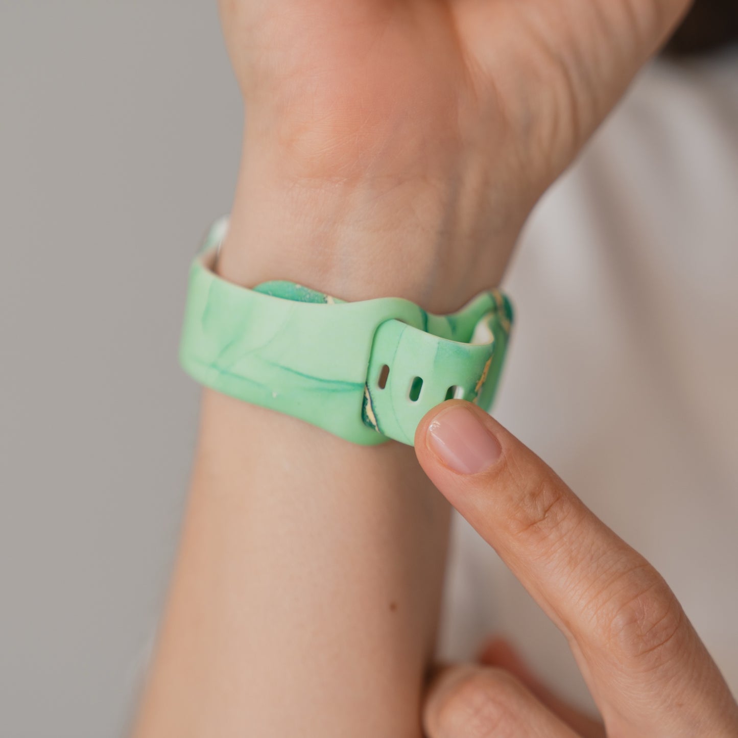 A hand befestigt ein arktisband Green Marble Apple Watch Armband am Handgelenk - das grüne Silikonarmband der Marke arktisband ist kompatibel mit der Apple Watch.