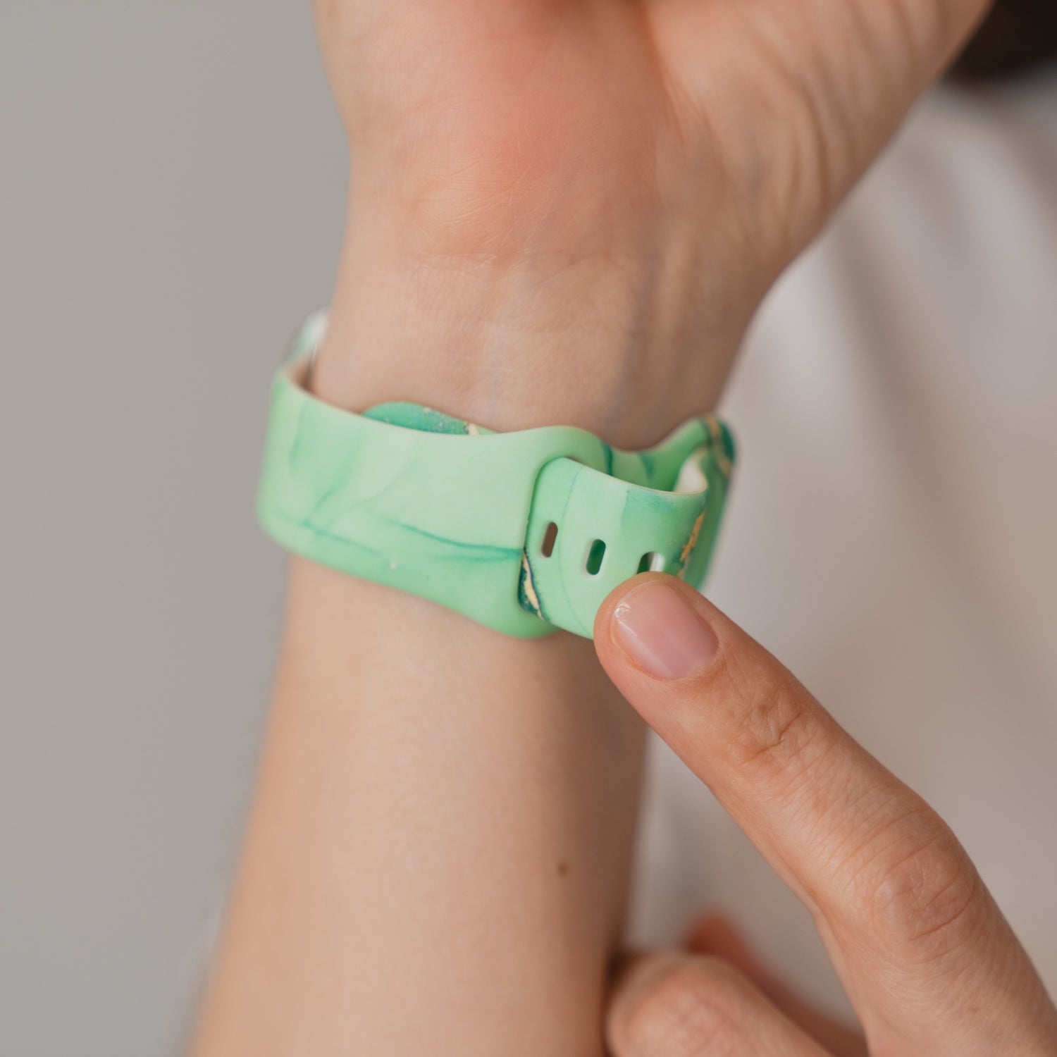 A hand befestigt ein arktisband Green Marble Apple Watch Armband am Handgelenk - das grüne Silikonarmband der Marke arktisband ist kompatibel mit der Apple Watch.