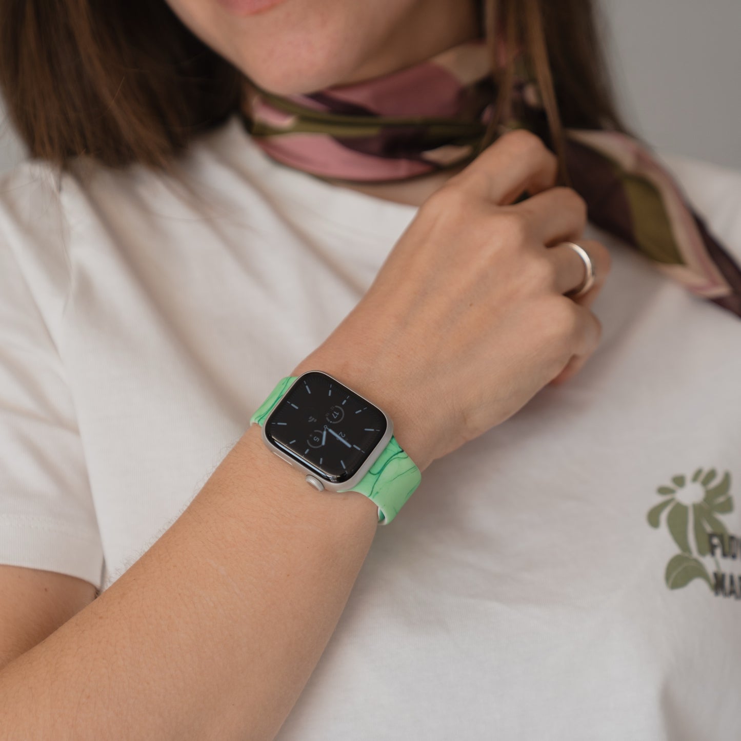 Eine Person, die ein arktisband Green Marble Apple Watch Armband und ein weißes T-Shirt trägt und einen gemusterten Schal hält.