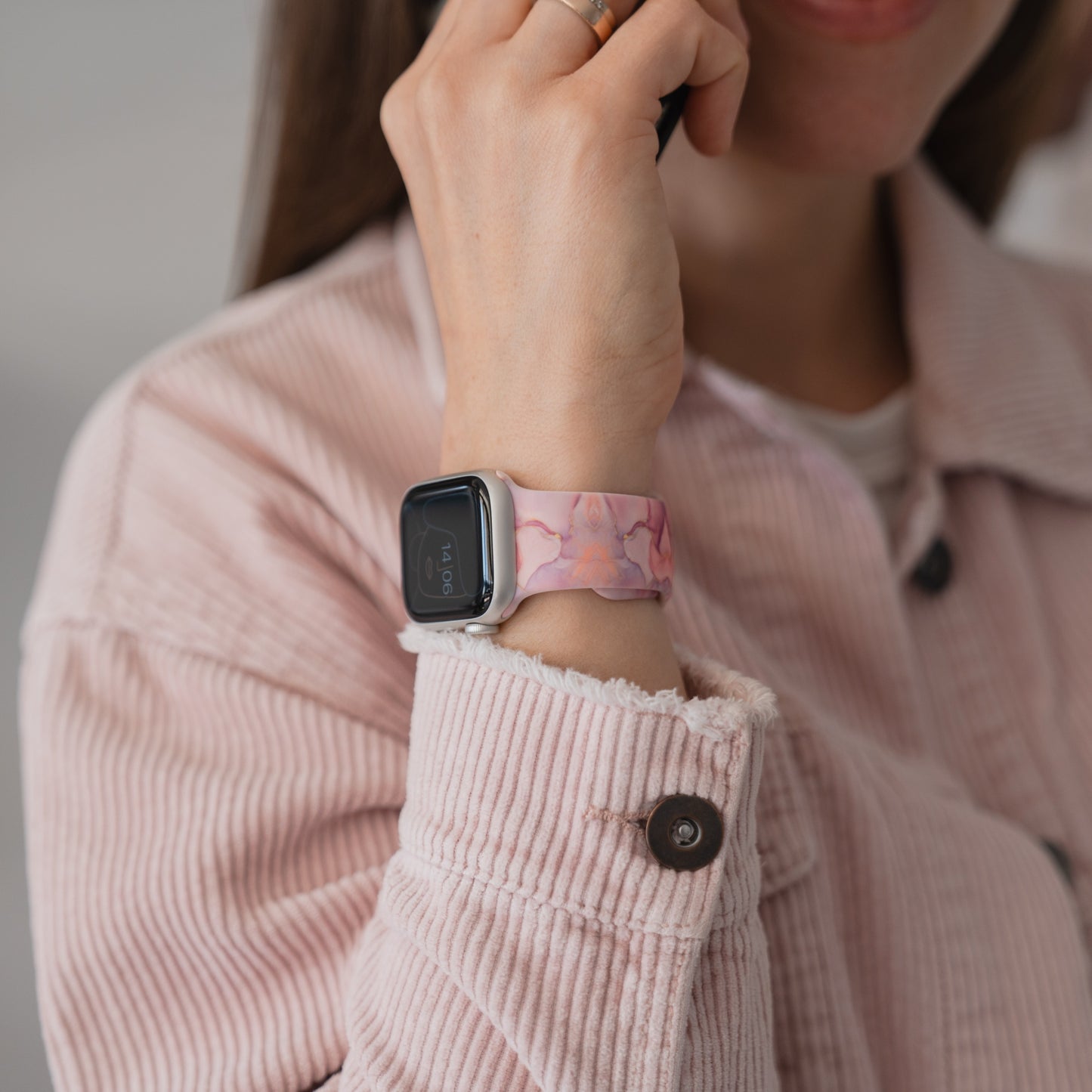 Lächelnde Frau in einer rosa Jacke trägt ein arktisband Rose Marble Apple Watch Armband von arktisband, das ihr Gesicht berührt.