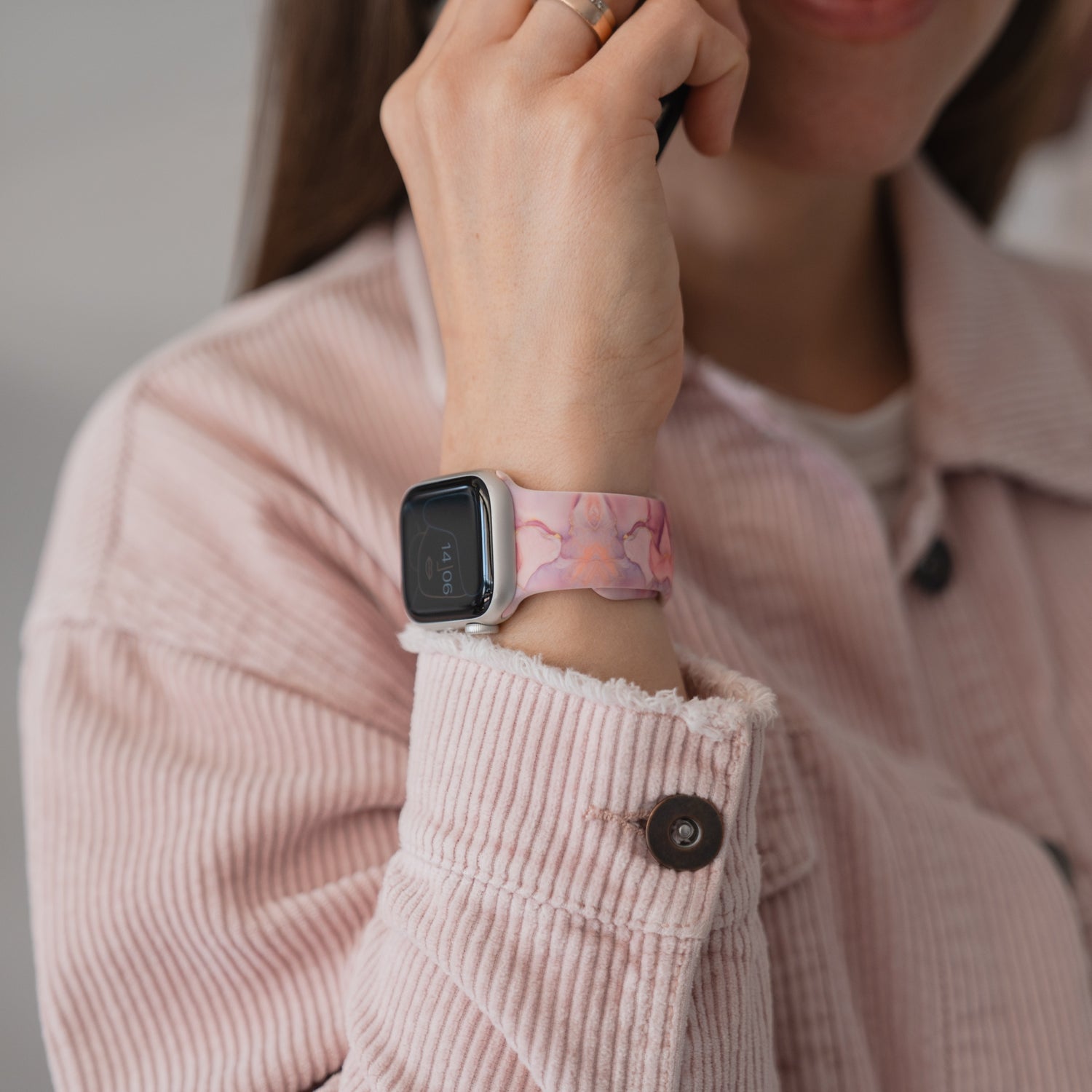 Lächelnde Frau in einer rosa Jacke trägt ein arktisband Rose Marble Apple Watch Armband von arktisband, das ihr Gesicht berührt.