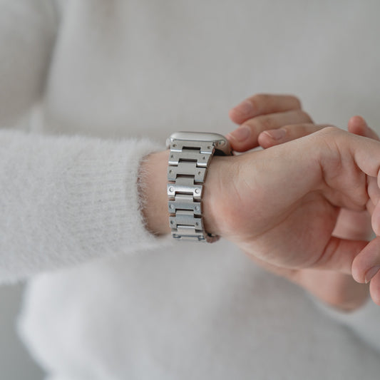 Eine Person in einem weißen Pullover überprüft die Uhrzeit auf einer Apple Watch mit dem Arktisband „Invictus“ Edelstahlarmband.