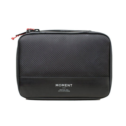 Die MOMENT Wetterfestes Mobile Lens Carrying Case für 4 Linsen ist eine schwarze rechteckige Reisetasche mit strukturierter Oberseite und Logo - ideal als Fototasche Outdoor mit Linsen Schutz für deine Ausrüstung.