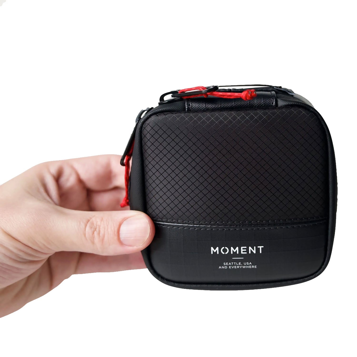 Eine Hand hält die MOMENT Wetterfestes Mobile Lens Carrying Case für 2 Linsen, eine kompakte schwarze Tasche mit strukturiertem Muster und roten Reißverschlussakzenten, die zuverlässigen Schutz für Ihre Fotoausrüstung bietet.