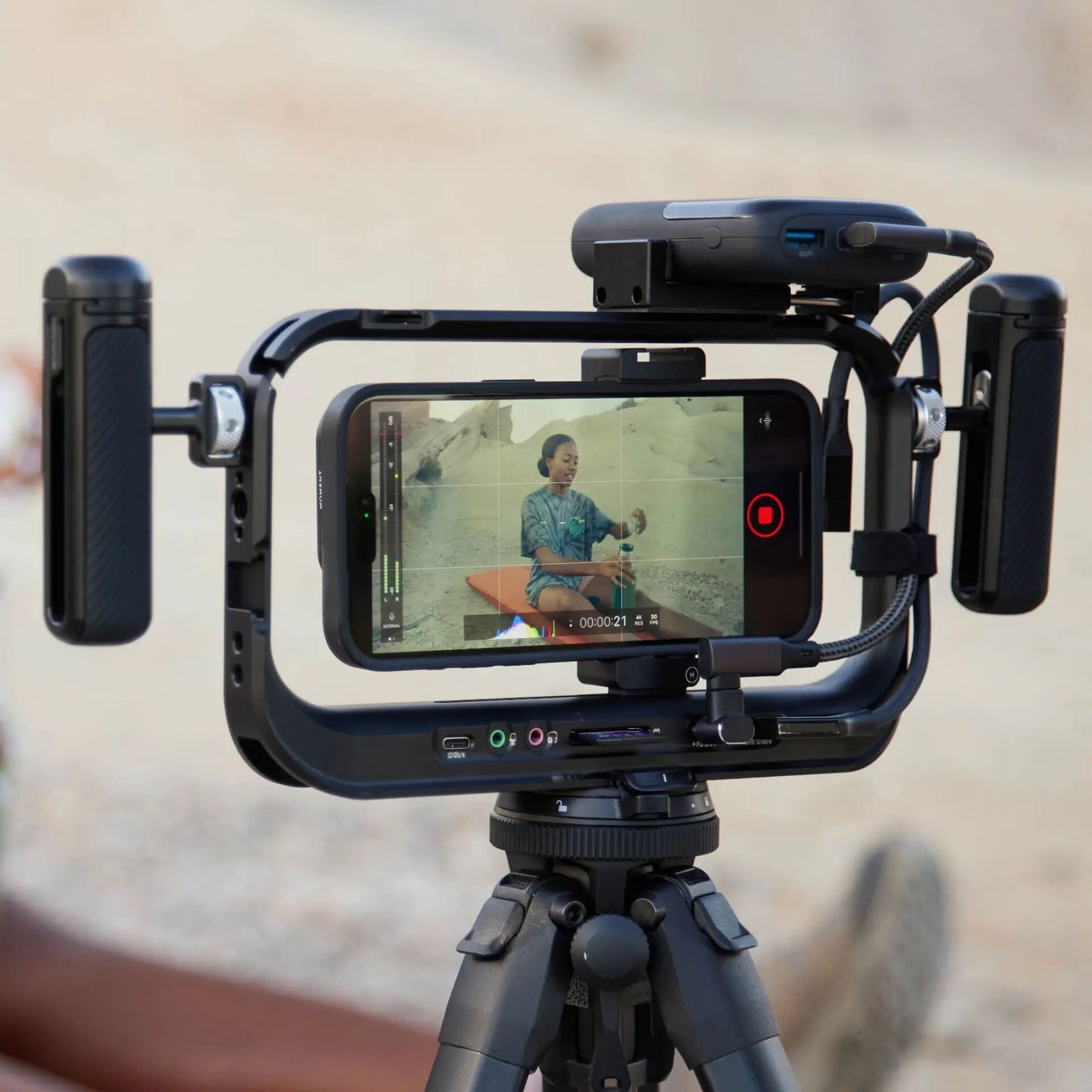 Eine Person sitzt im Freien und wird von einem Smartphone mit dem MOMENT Supercage mit USB-C Hub auf einem Stativ gefilmt - die ideale Ausrüstung für jeden iPhone-Filmemacher, der kreative Momente festhalten möchte.