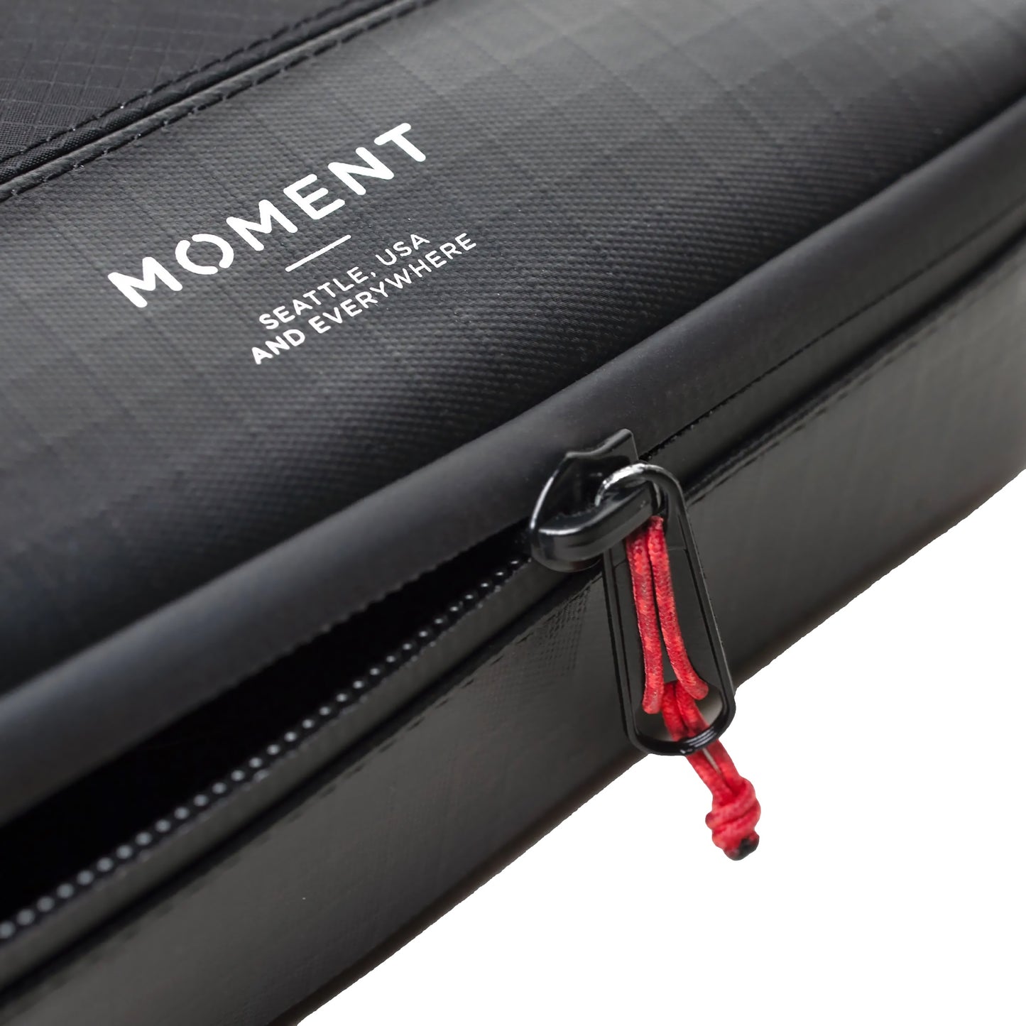 Nahaufnahme der schwarzen MOMENT Wetterfestes Mobile Lens Carrying Case für 4 Linsen mit roten Reißverschlüssen und weißem MOMENT Logo - ideal zum Schutz Ihres wetterfesten Kamerazubehörs.