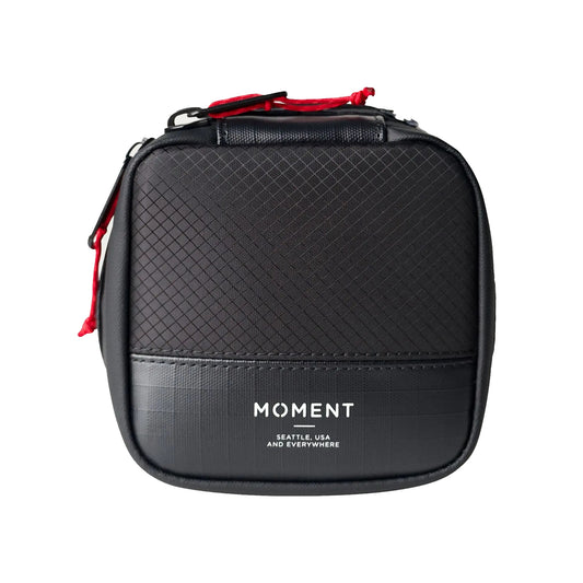 Das MOMENT Wetterfestes Mobile Lens Carrying Case für 2 Linsen ist ein kleines, schwarzes Case mit Textur und Front-Branding. Es schützt deine Fotoausrüstung dank gepolsterter Objektivtasche optimal vor Nässe und Stößen.