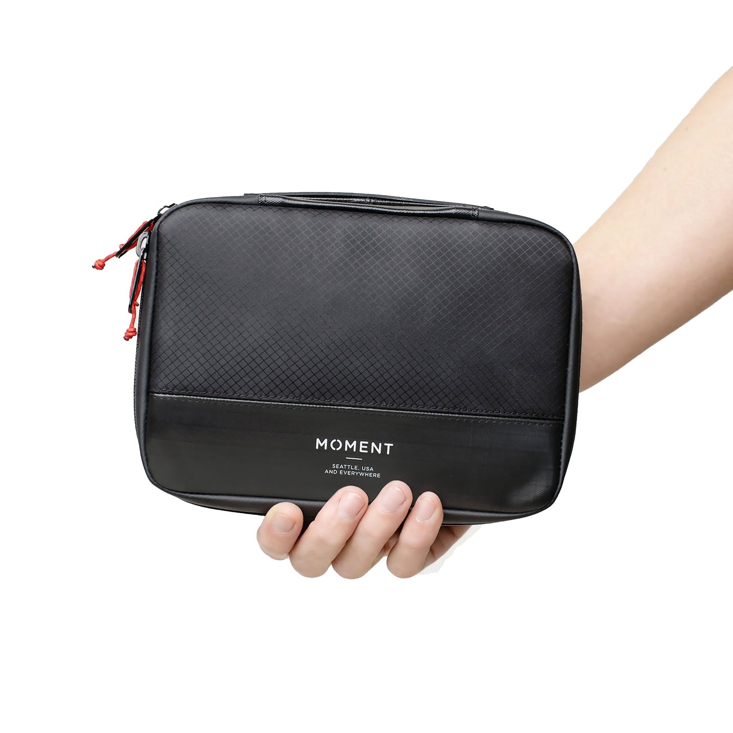 Eine Hand hält die schwarze MOMENT Wetterfestes Mobile Lens Carrying Case für 4 Linsen mit einer Reißverschlusstasche mit MOMENT Branding vor einem weißen Hintergrund.