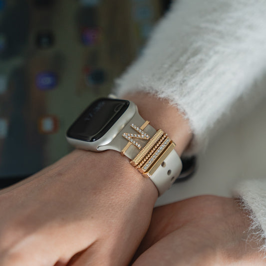 Eine Smartwatch am Handgelenk mit Arktisband Apple Watch Charms „N Style“, die das weiße Band zieren.