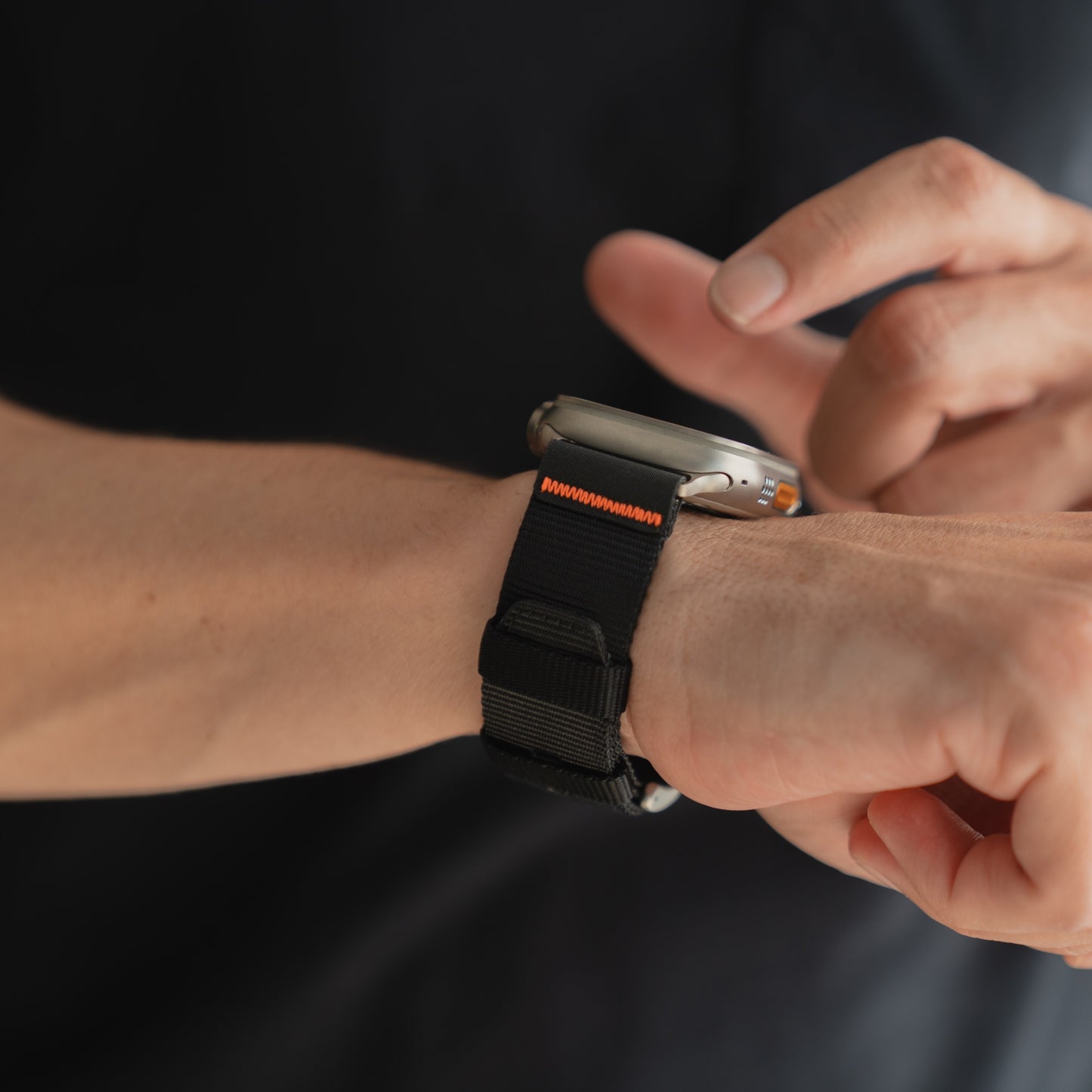 Eine Person tippt sich ein arktisband Apple Watch Armband "Terra" mit einem schwarz-orangen extrabreiten 24 mm Nylonband um das Handgelenk.