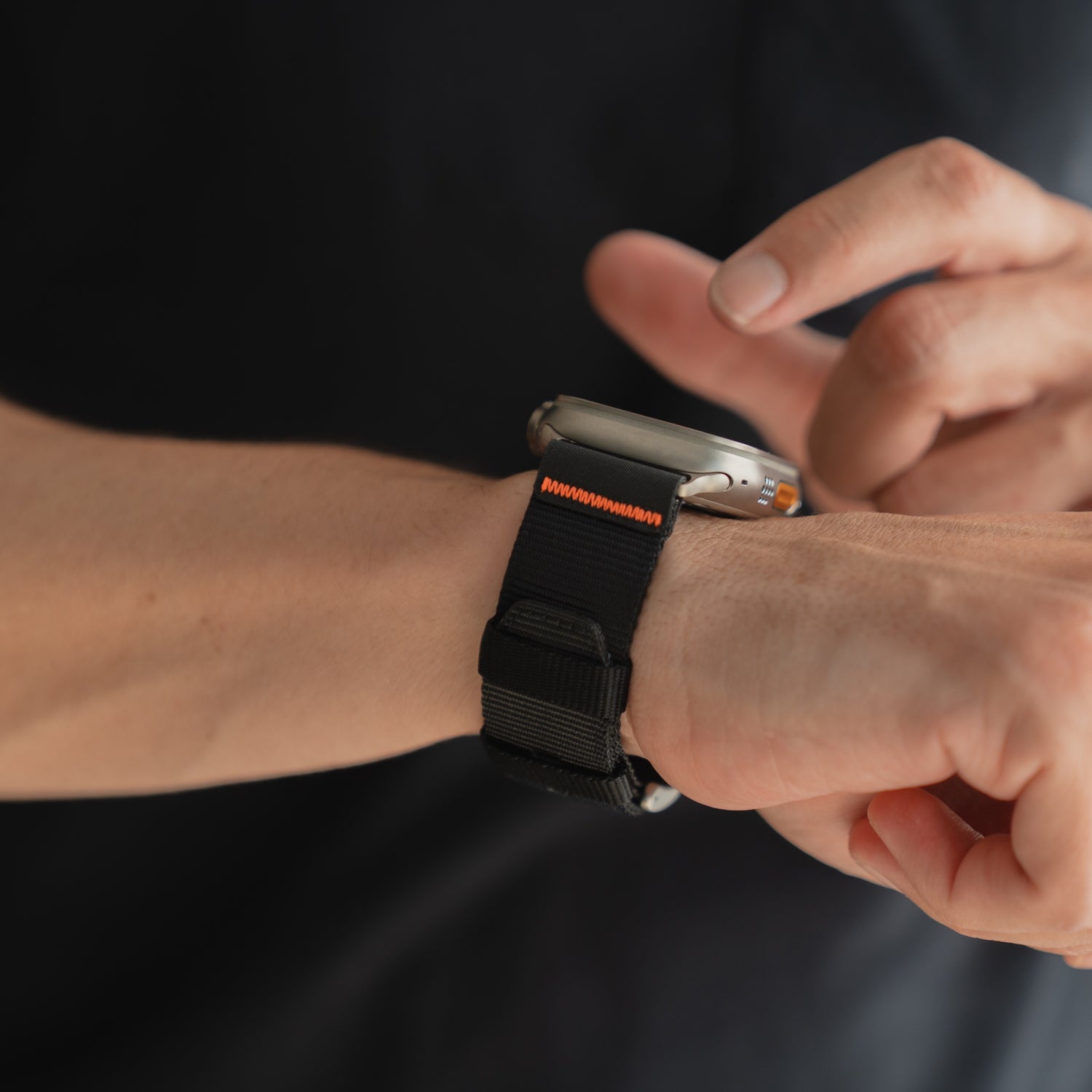 Eine Person tippt sich ein arktisband Apple Watch Armband "Terra" mit einem schwarz-orangen extrabreiten 24 mm Nylonband um das Handgelenk.
