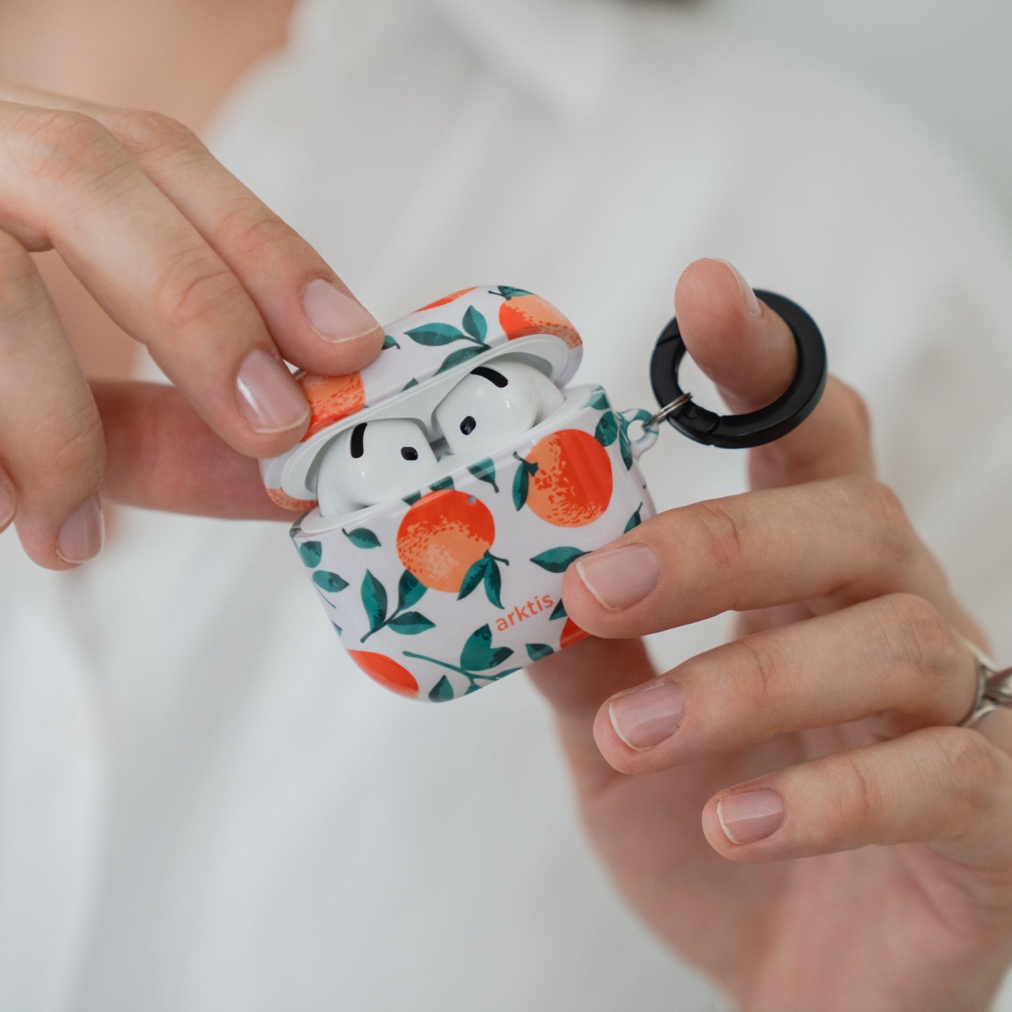 Hände, die eine Arktis AirPods 4-Hülle – Orange Tree-Hülle mit schwarzem Ring – öffnen.