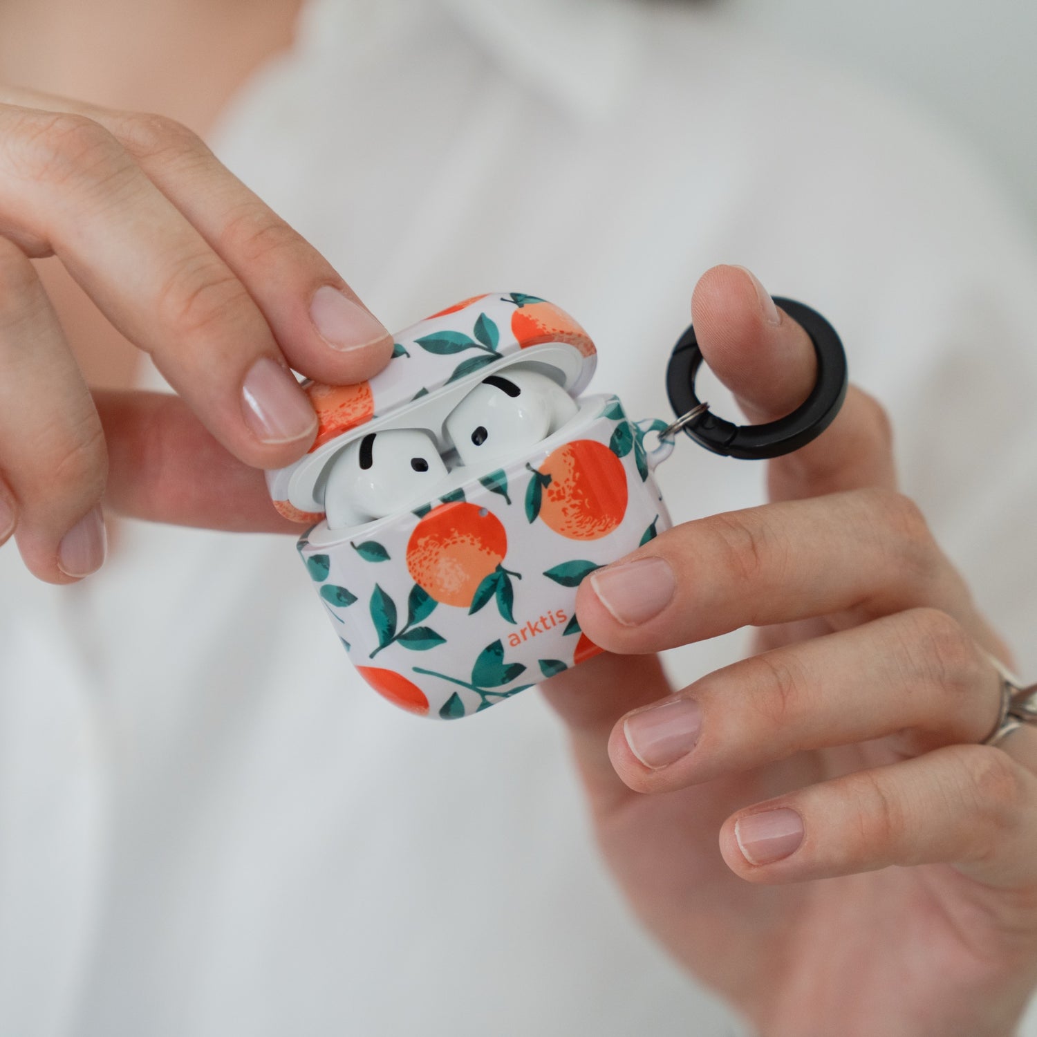 Hände, die eine Arktis AirPods 4-Hülle – Orange Tree-Hülle mit schwarzem Ring – öffnen.
