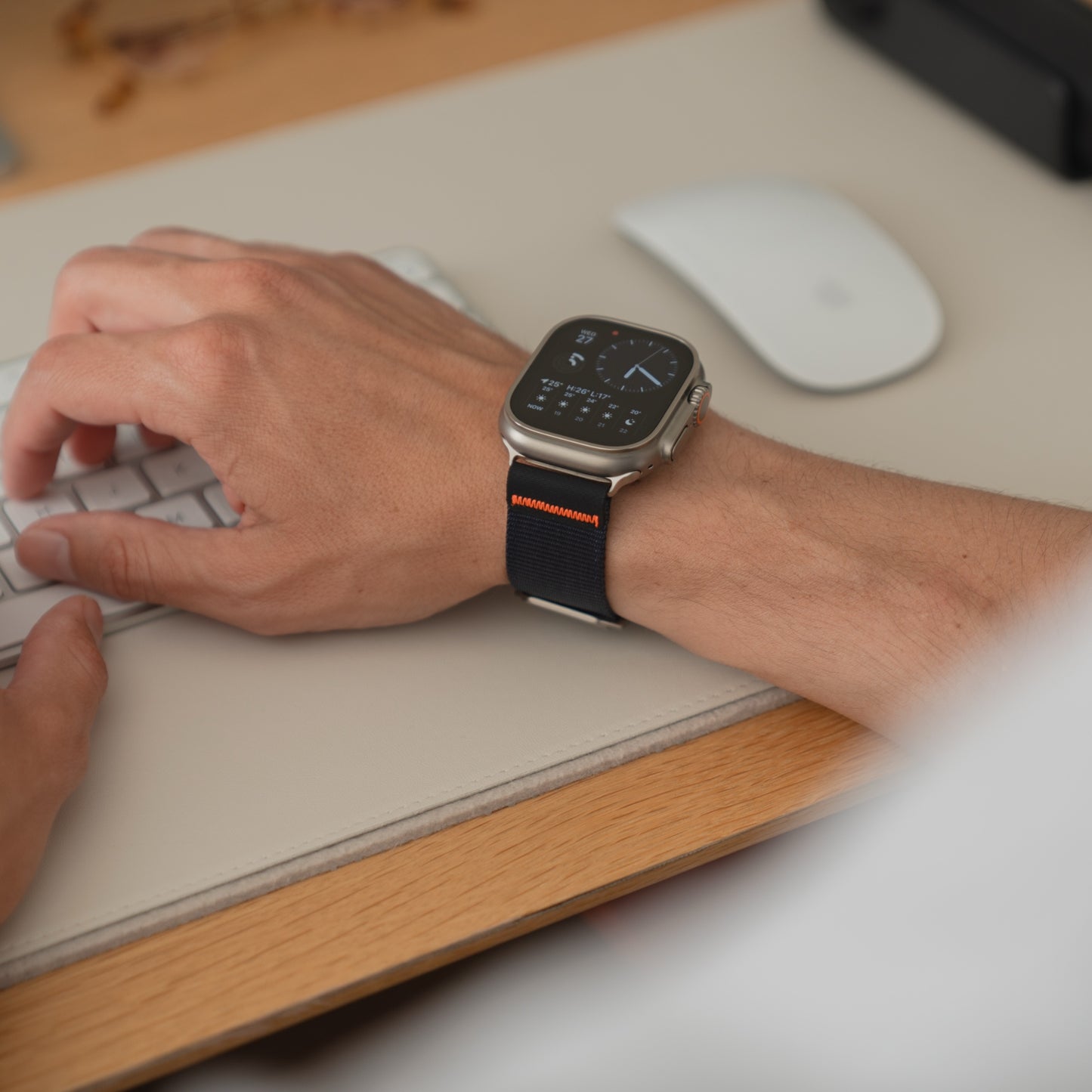 Jemand trägt ein arktisband Apple Watch Armband "Terra" von arktisband mit einem extrabreites 24 mm Nylonband und tippt auf einer Tastatur an einem Schreibtisch mit einer Maus in der Nähe.