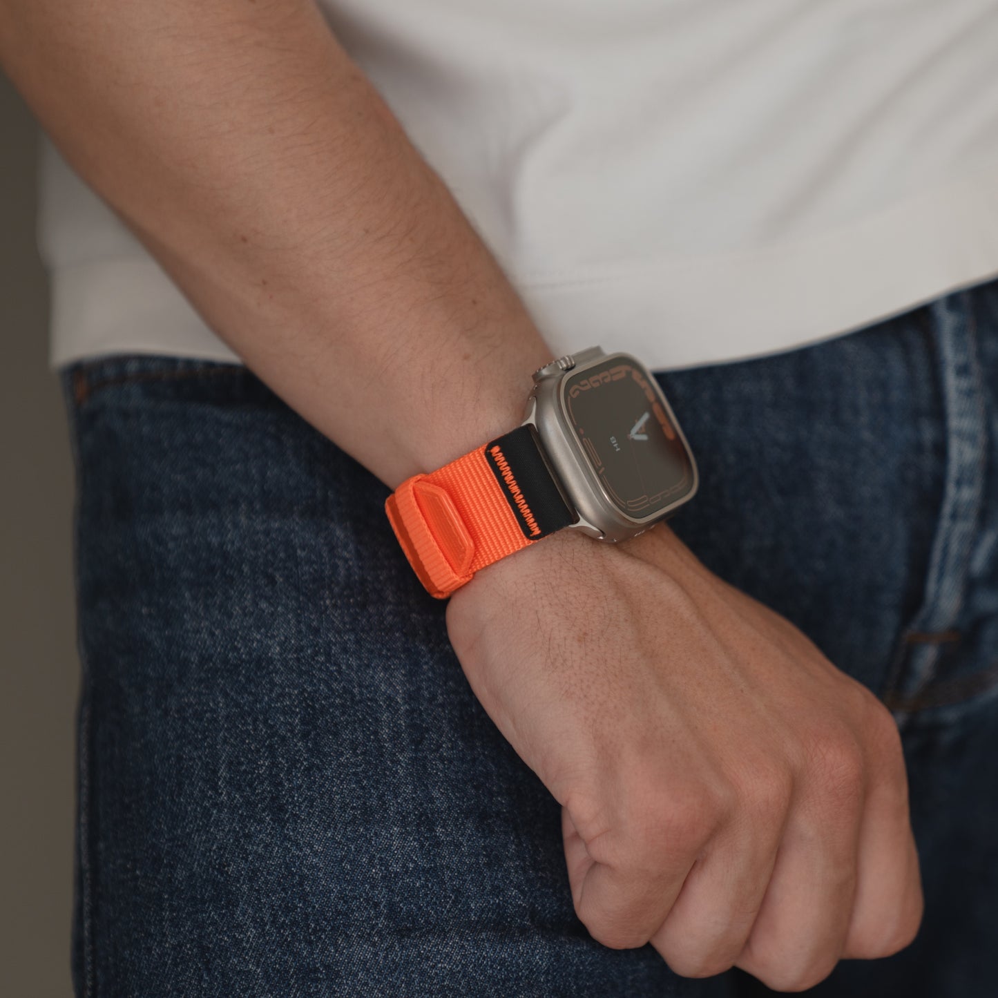Eine Person trägt ein arktisband Apple Watch Armband "Terra" von arktisband in Orange und Schwarz an ihrer Apple Watch Ultra, gepaart mit einem weißen Hemd und einer blauen Jeans.