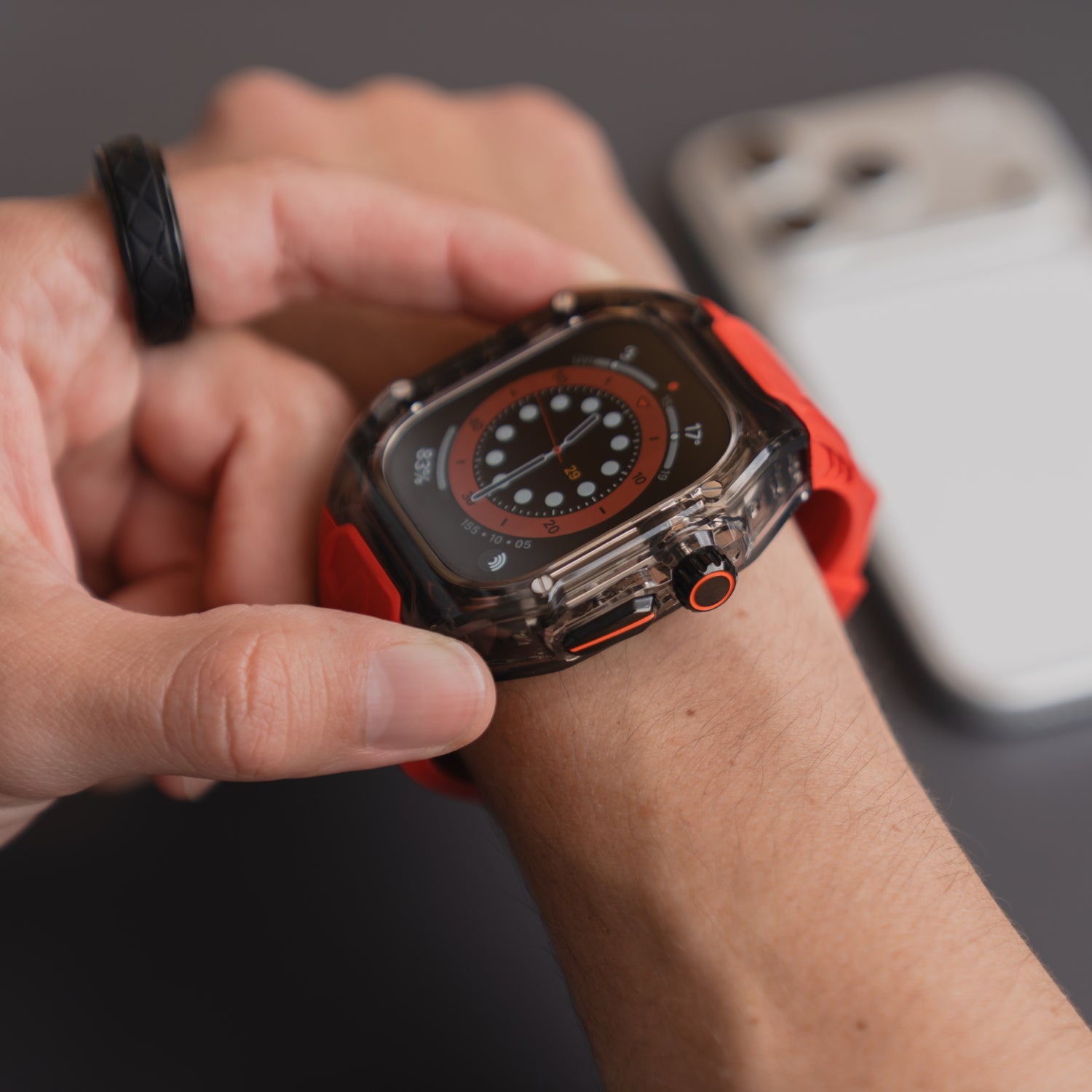 Nahaufnahme einer Person, die das arktisband Apple Watch Armband "Armor Fusion" von arktisband mit rotem Silikonband trägt, den Bildschirm berührend, Telefon im Hintergrund.