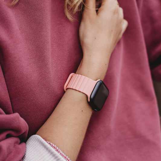 Eine Person trägt das arktisband Apple Watch Magnetarmband „Neo“ von arktisband in Pink am linken Handgelenk, kombiniert mit einem malvenfarbenen Langarmshirt.