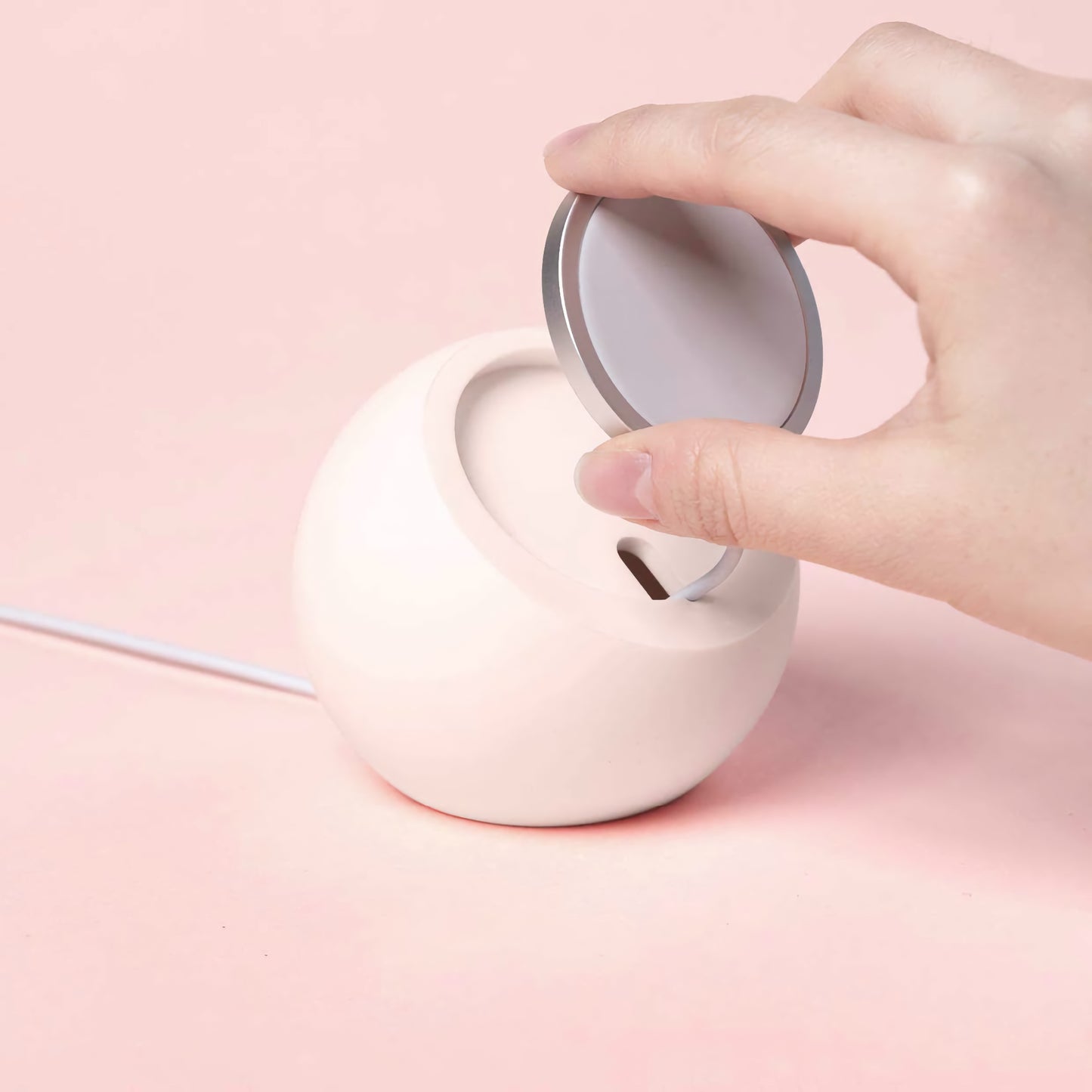 Eine Hand platziert ein rundes Gerät auf dem arktis MagSafe Orbit Stand, einer weißen, kugelförmigen Ladestation von arktis für kabelloses Laden, vor einem rosa Hintergrund.