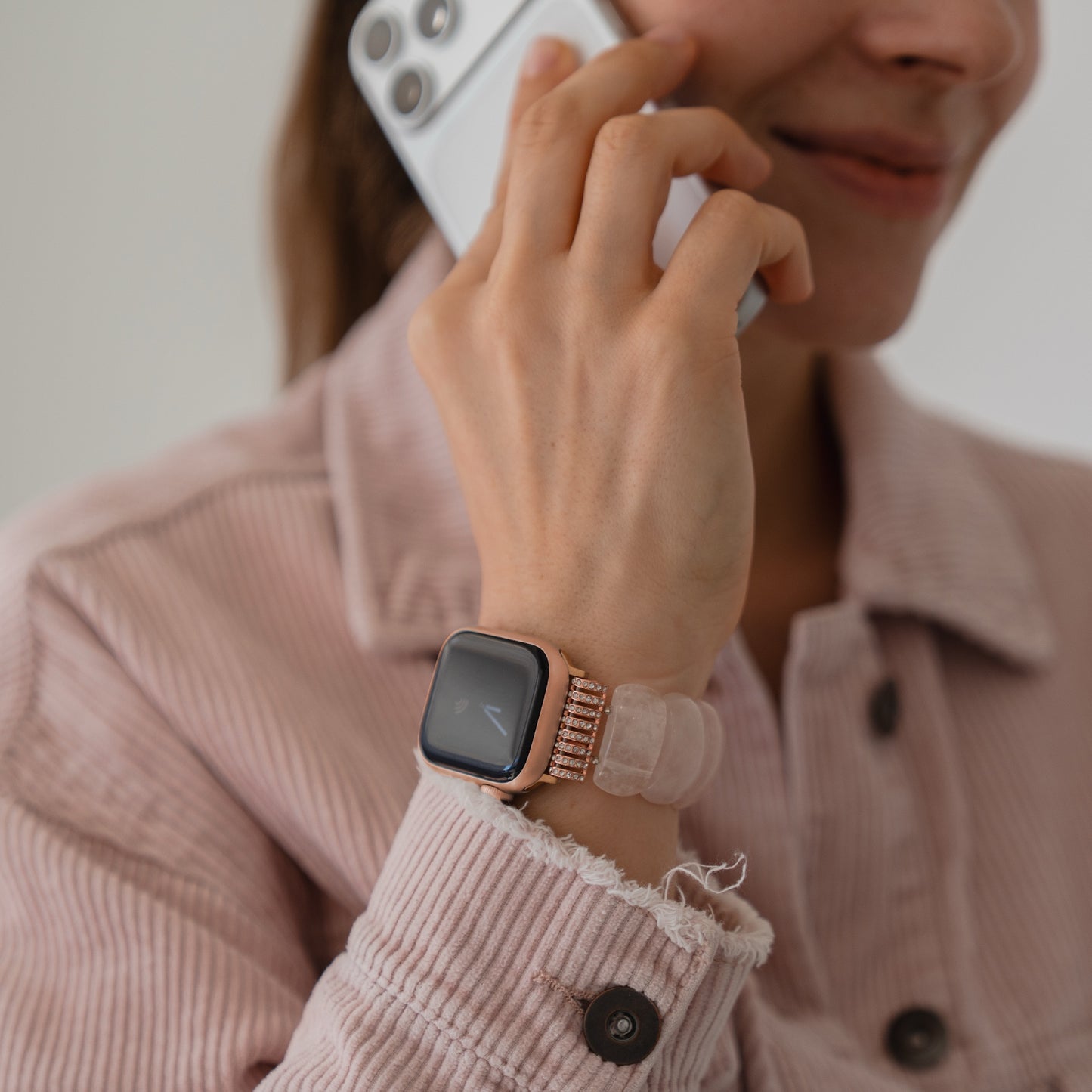 Eine Frau in einer rosafarbenen Jacke telefoniert, während sie das arktisband Apple Watch "Stone Pearl" Armband mit elastischem Verschluss am Handgelenk trägt.