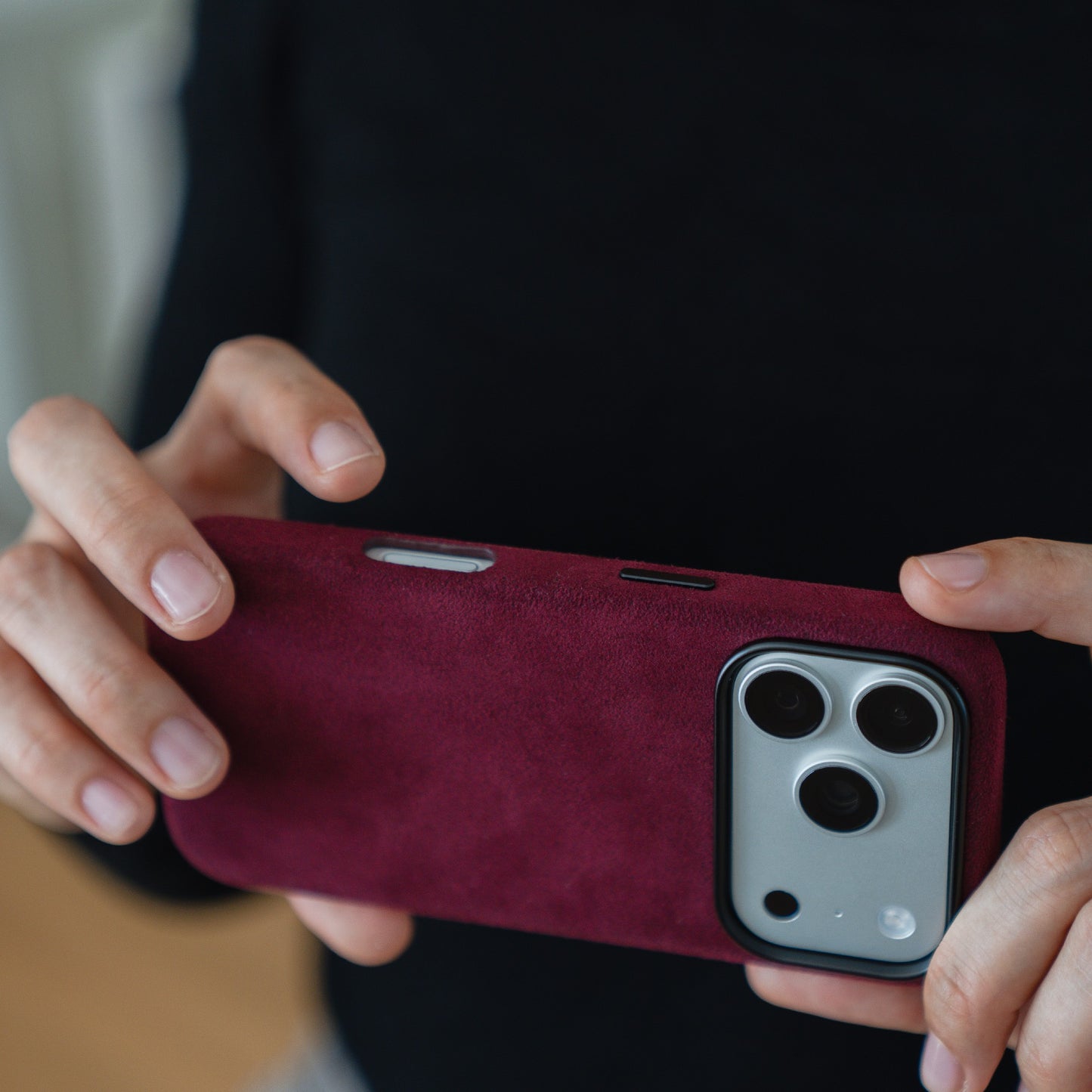 Eine Person hält eine arktis iPhone 17 Pro Hülle aus Alcantara in kastanienbraun, die Kameralinsen sind sichtbar, und trägt ein schwarzes Oberteil.