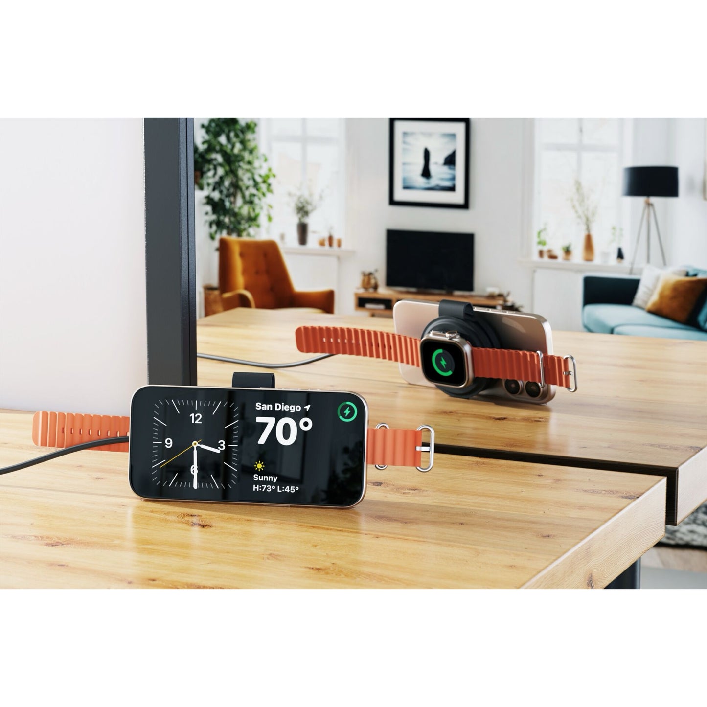 Ein Satechi OntheGo 2-in-1 Wireless Charger von Satechi lädt eine MagSafe-kompatible Smartwatch und ein Smartphone auf einem Holztisch neben einem Spiegel in einem modernen Raum.