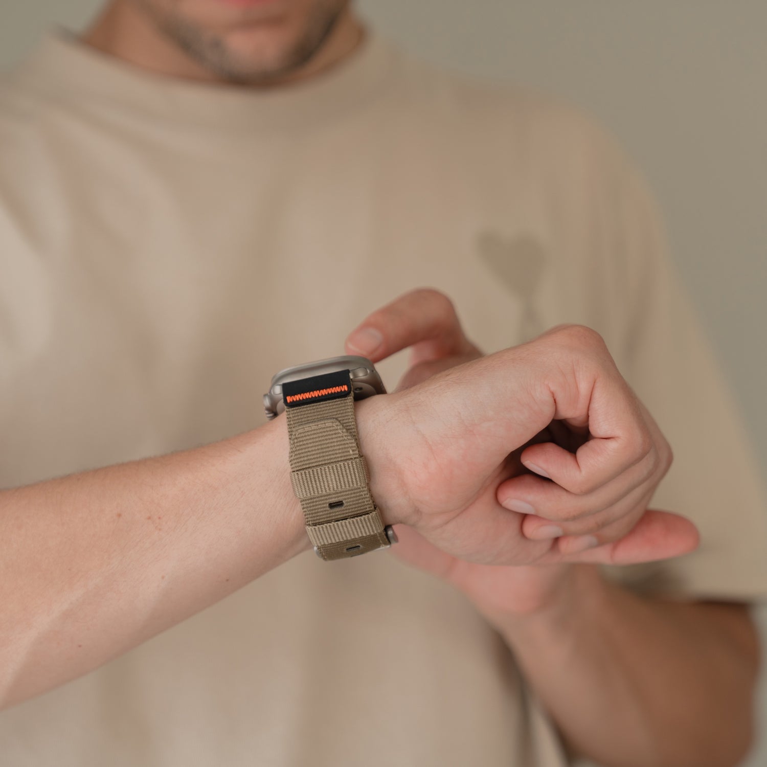 Eine Person in einem beigen Hemd kontrolliert ihre Apple Watch Ultra, die mit dem arktisband "Terra" 24 mm Nylonband von arktisband ausgestattet ist.