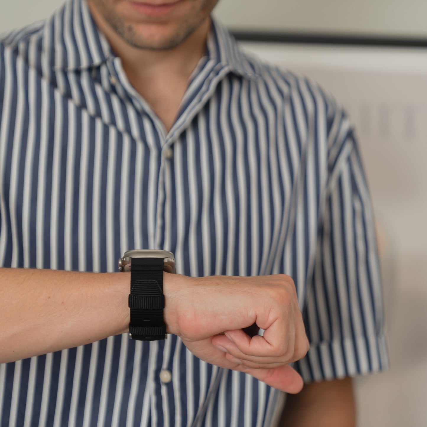 Eine Person in einem gestreiften Hemd schaut auf ihr arktisband Apple Watch Armband "Terra" (Marke: arktisband) am Handgelenk.