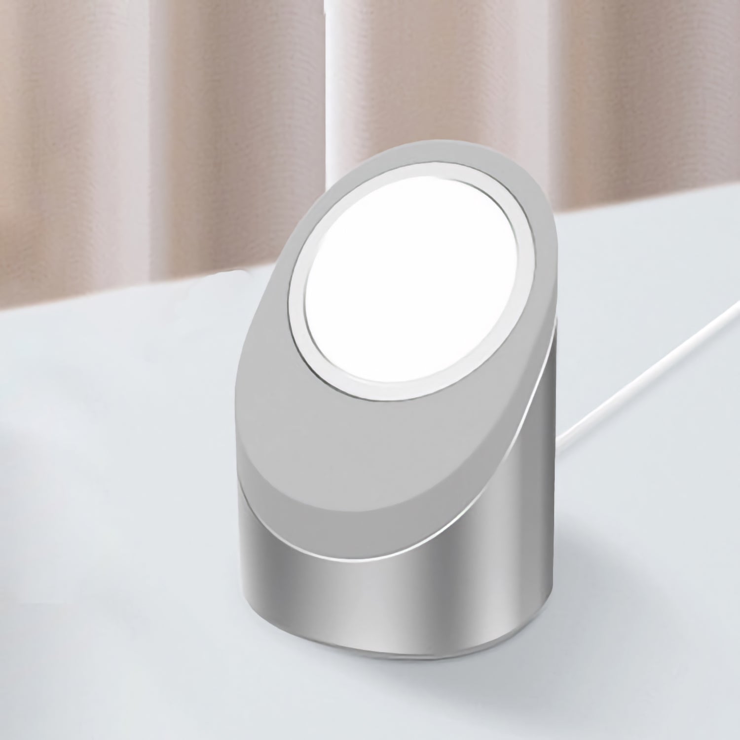 Das kabellose Ladegerät arktis MagSafe NightStand von arktis in modernem Silber steht auf einer weißen Fläche neben beigen Vorhängen.