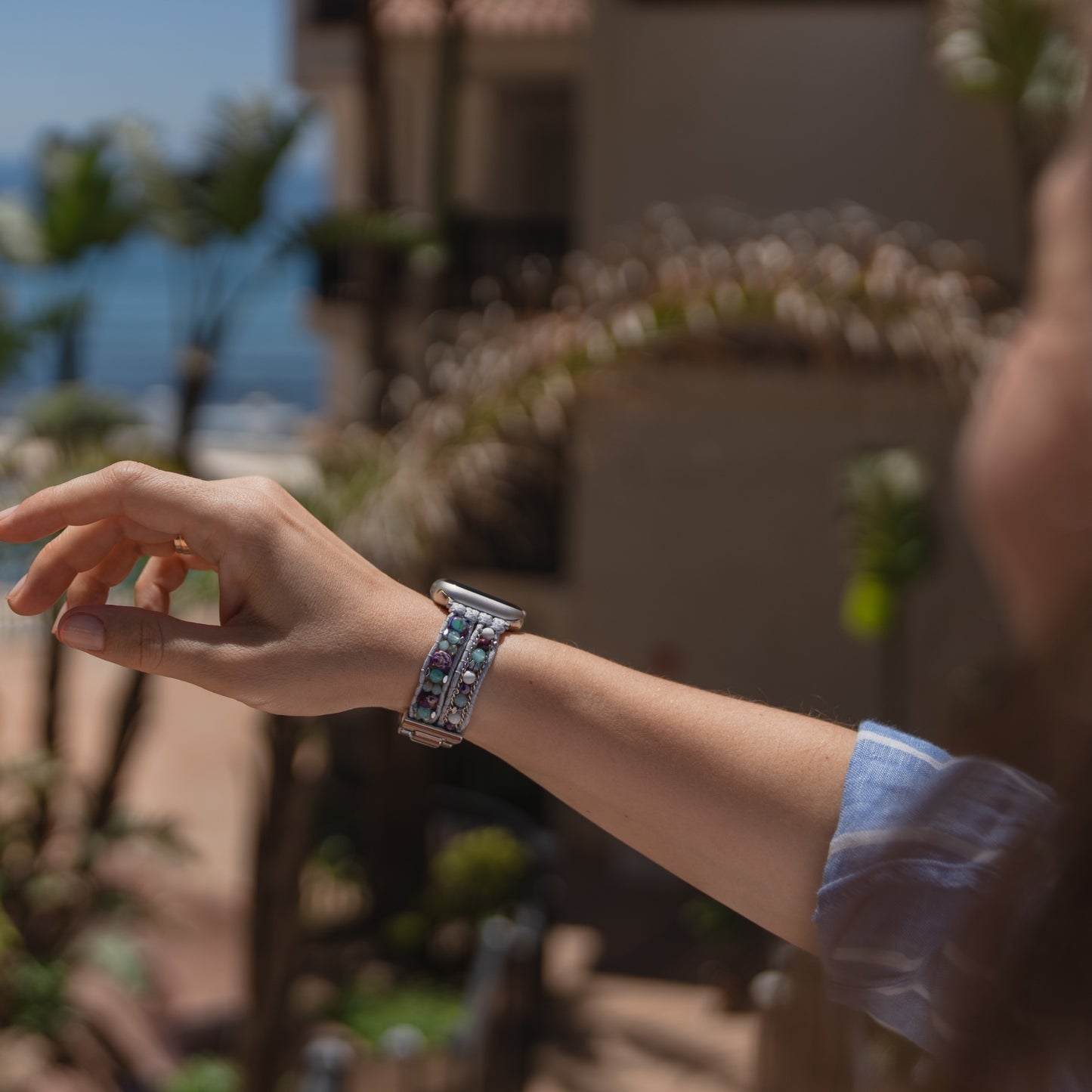 Jemand, der das Apple Watch-Armband „Sunset Spirit“ von arktisband trägt, hebt im Freien den Arm, im Hintergrund sind Palmen und Gebäude zu sehen.