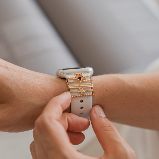 Eine Person passt das Armband ihrer Apple Watch an, das über arktisband Apple Watch Charms „Star“ in Gold auf einem weißen Band verfügt.