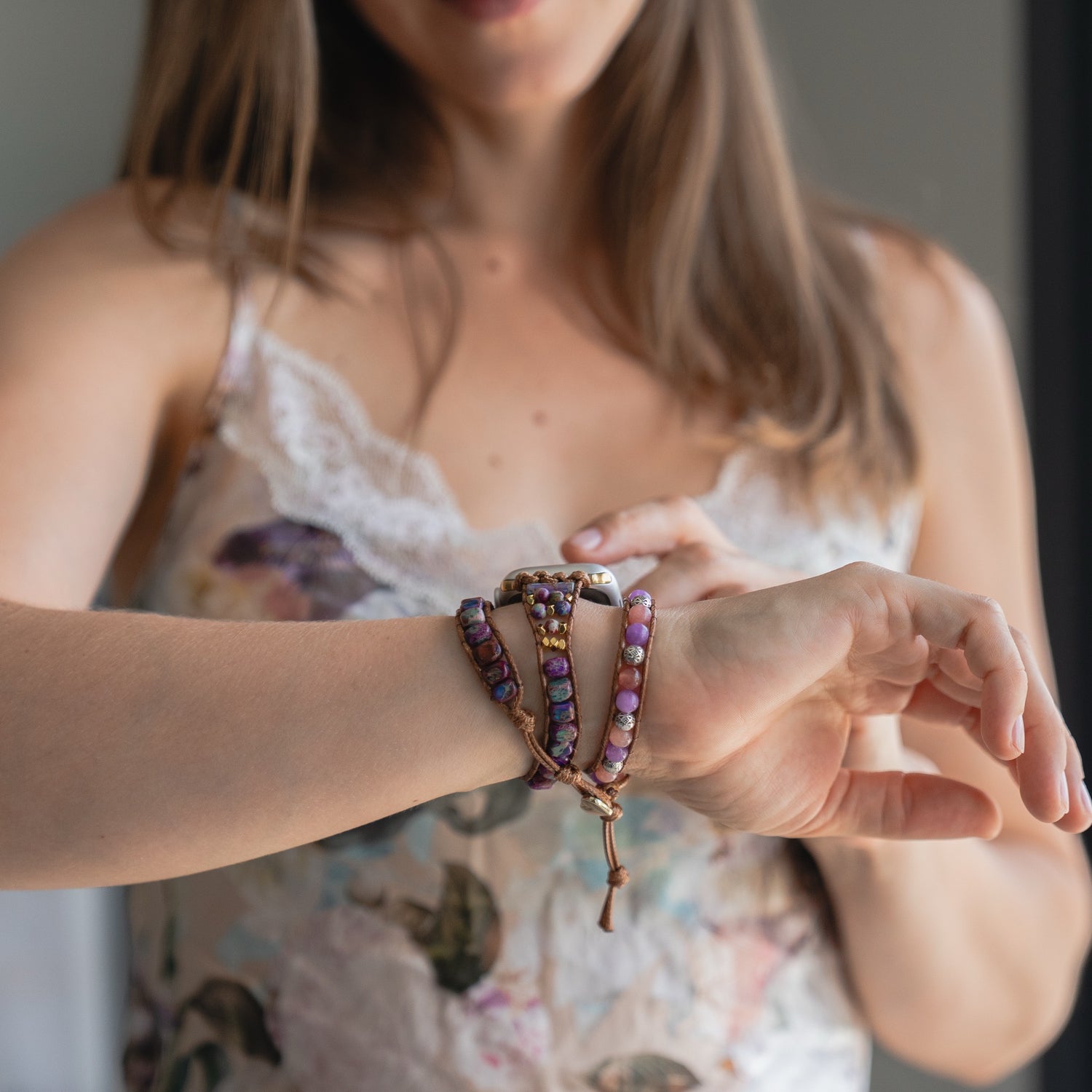 Eine Frau in einem geblümten Kleid präsentiert das arktisband Apple Watch Armband "Dream Catcher" von arktisband an ihrem Handgelenk und stellt es mit der anderen Hand ein.