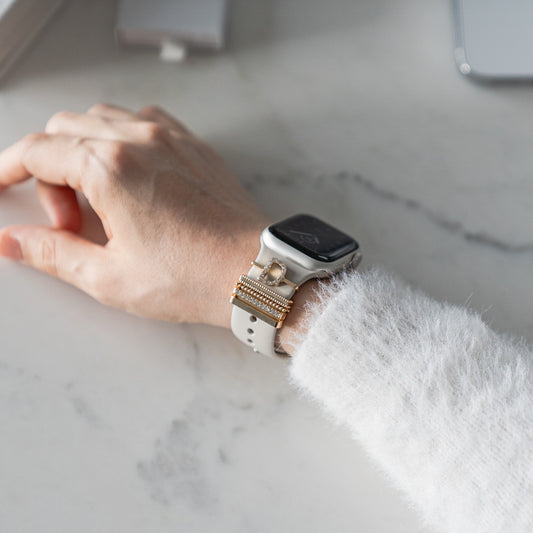 Eine mit den Arktisband Apple Watch Charms „D Style“ geschmückte Hand ruht elegant auf weißem Marmor und verleiht dem Accessoire einen schicken Touch.